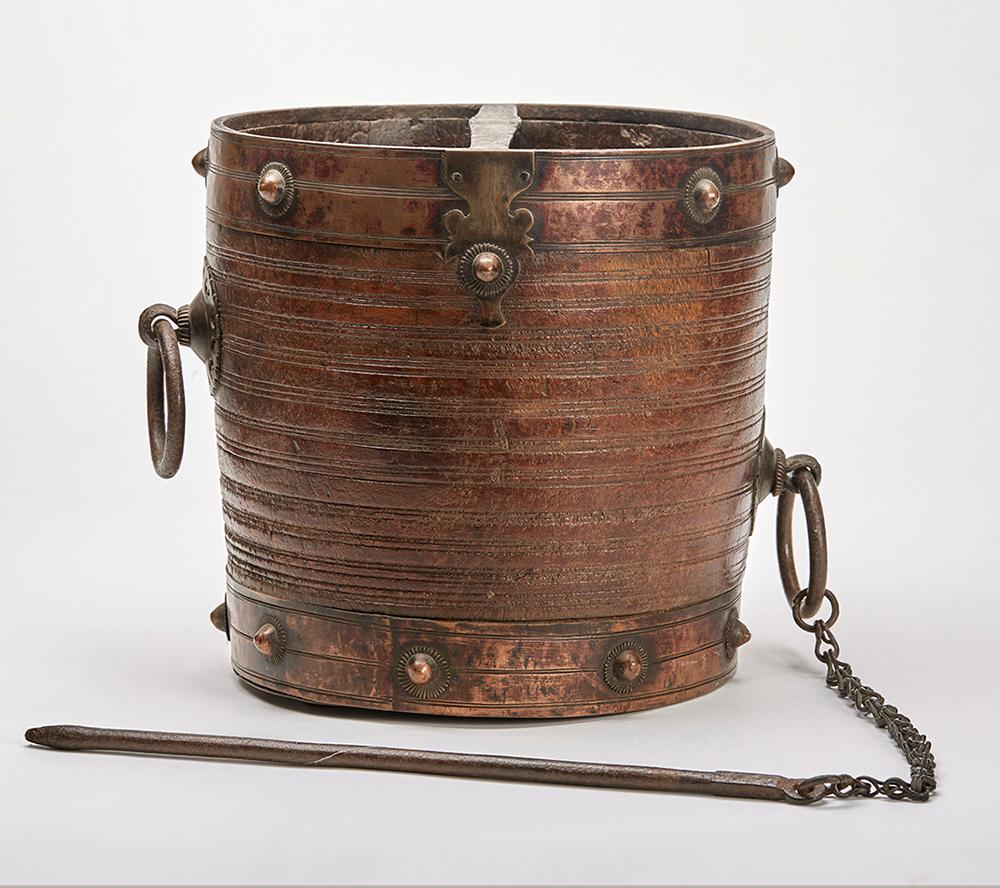 A fine and unusual antique metal clad and mounted wooden rice or grain bucket with attached steel poker originating from Southern India. The twin handled bucket is carved from a solid hand turned block of tropical hard wood with brass banding with