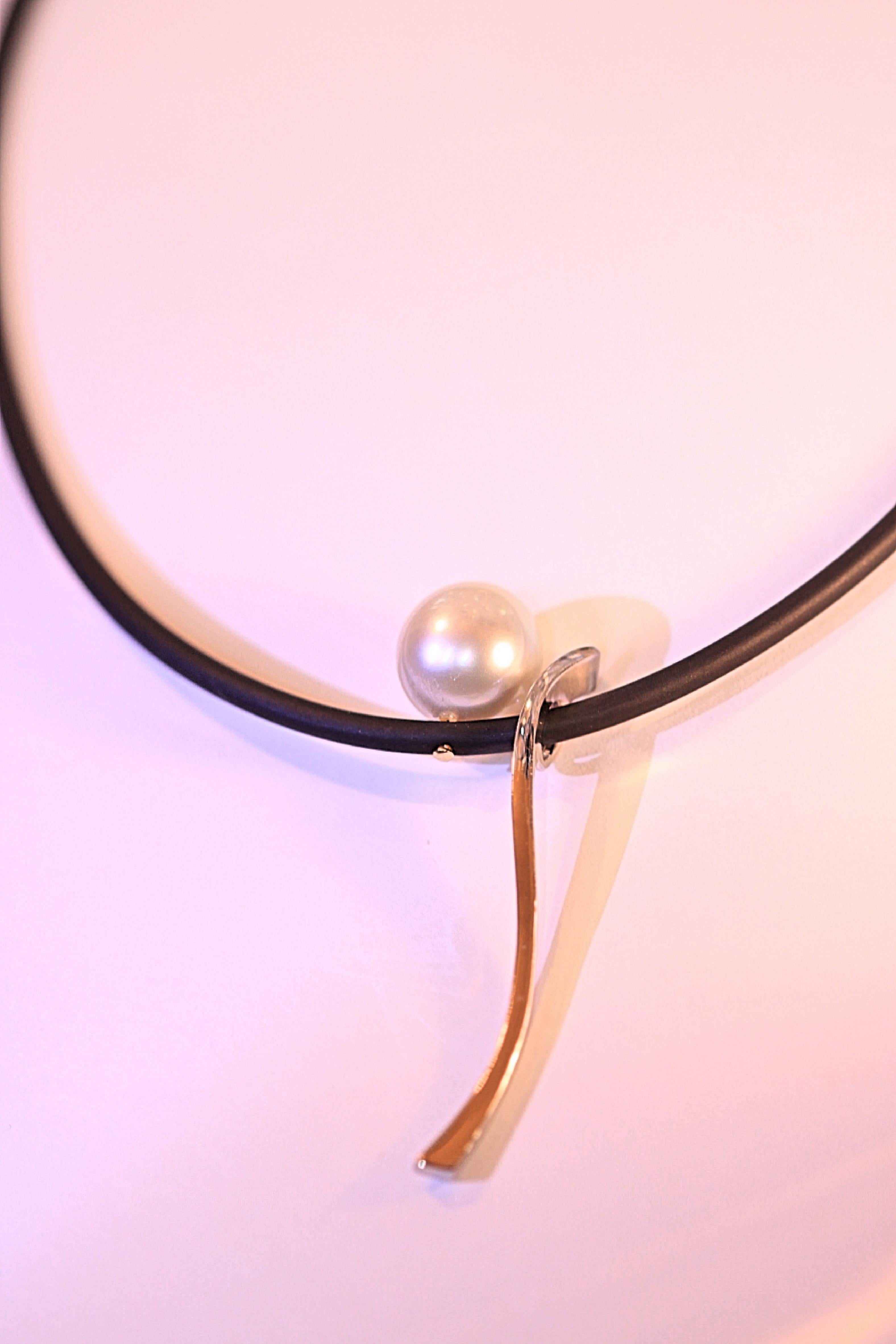 A  classy pearl, white gold and black cord necklace.  The pearl is a 13 mm round, beautiful pearl that has excellent luster and minor blemishes.  The pearl is attached to a black cord and the cord has a 14 karat white gold dangle next to the pearl. 
