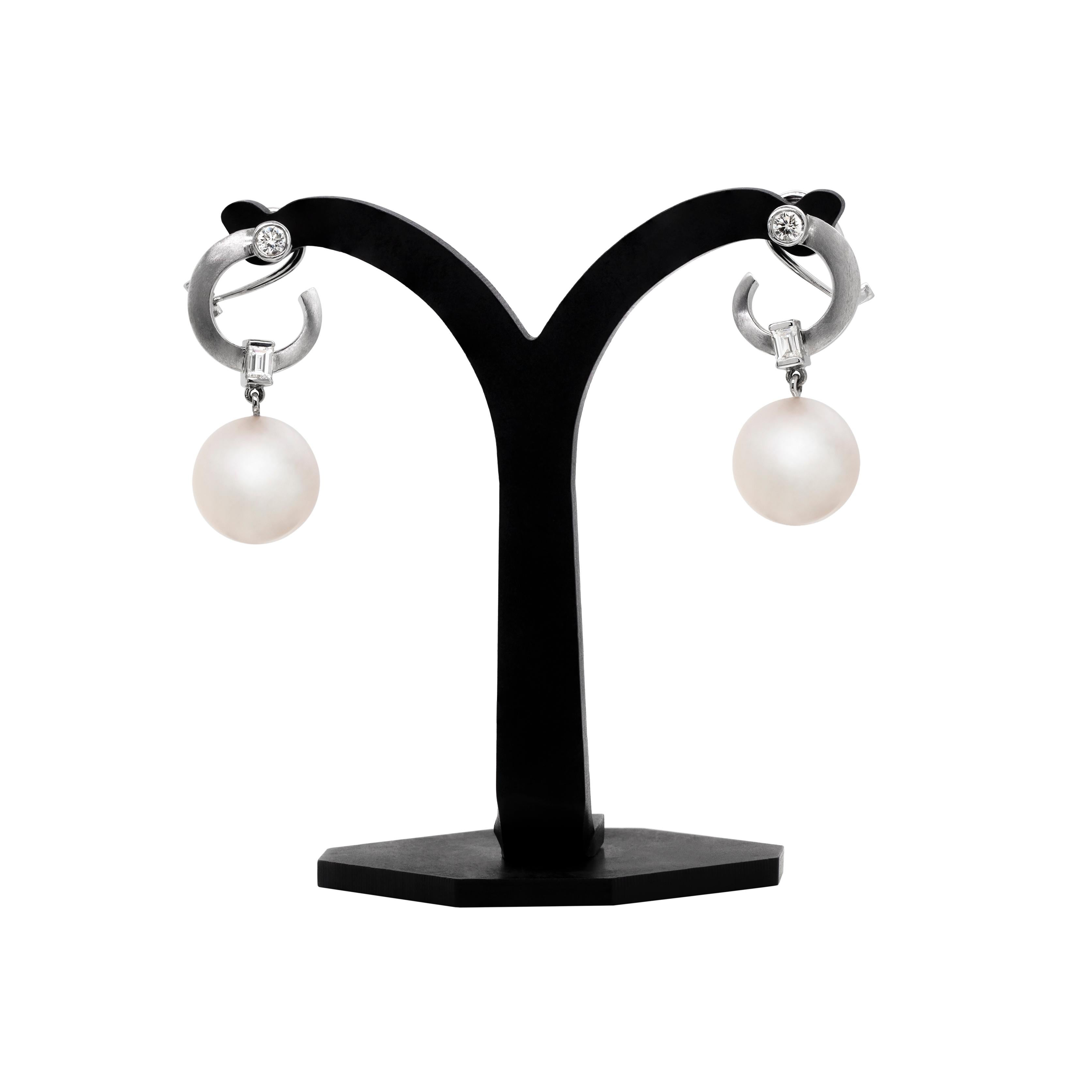 These gorgeous dress earrings are made in 18 carat white gold, each featuring a South Sea cultured pearl measuring 12.4mm, suspended below tapering hoops with a matte textured finish, accented by a round brilliant cut and baguette cut diamonds