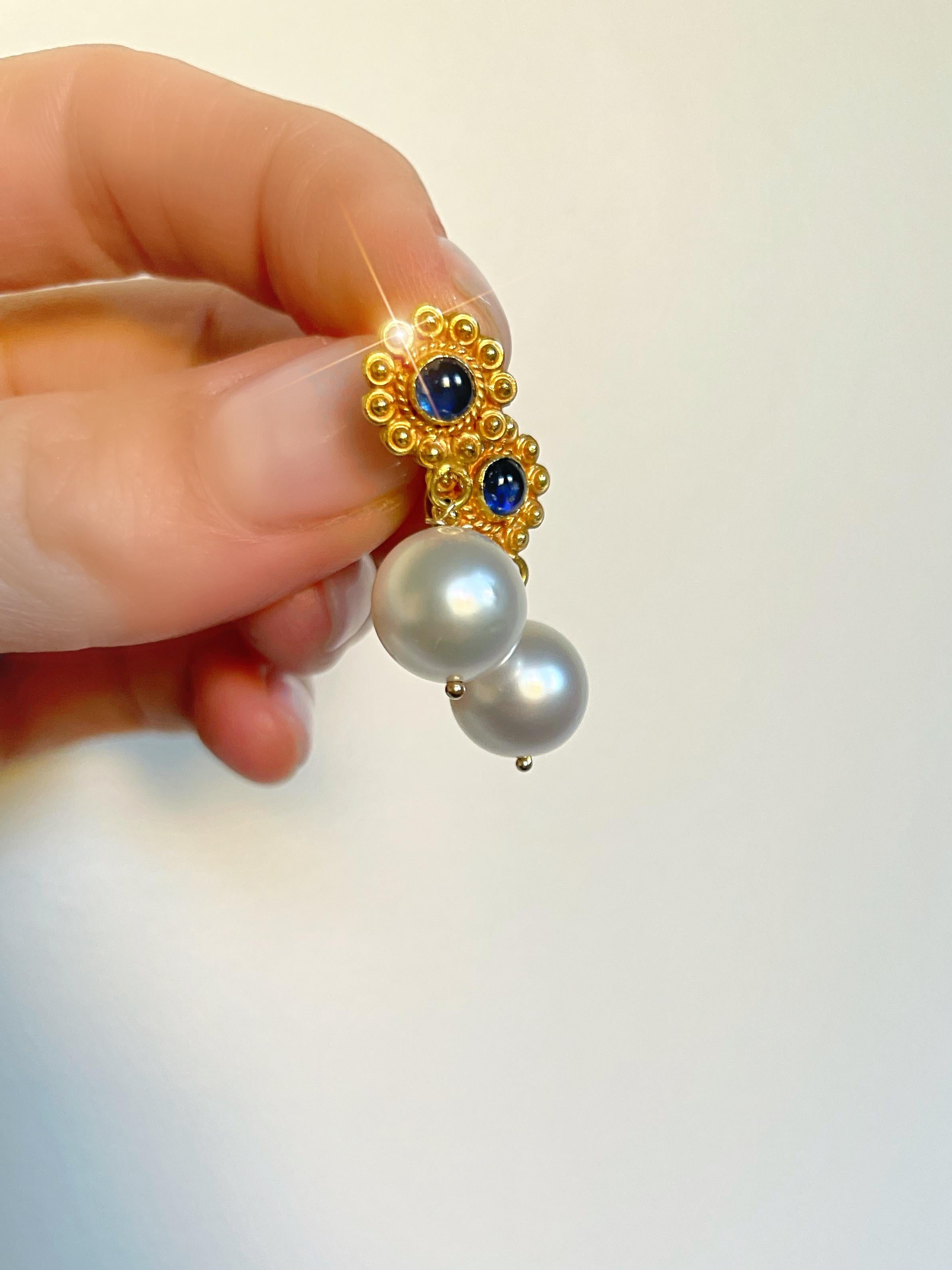 Set in rich 18k yellow gold with elegantly designed post-back closures, framing two perfectly matched blue sapphire cabochons. Completing the design are 2 lustrous South Sea pearls suspended to give just the right movement to the earring. No detail