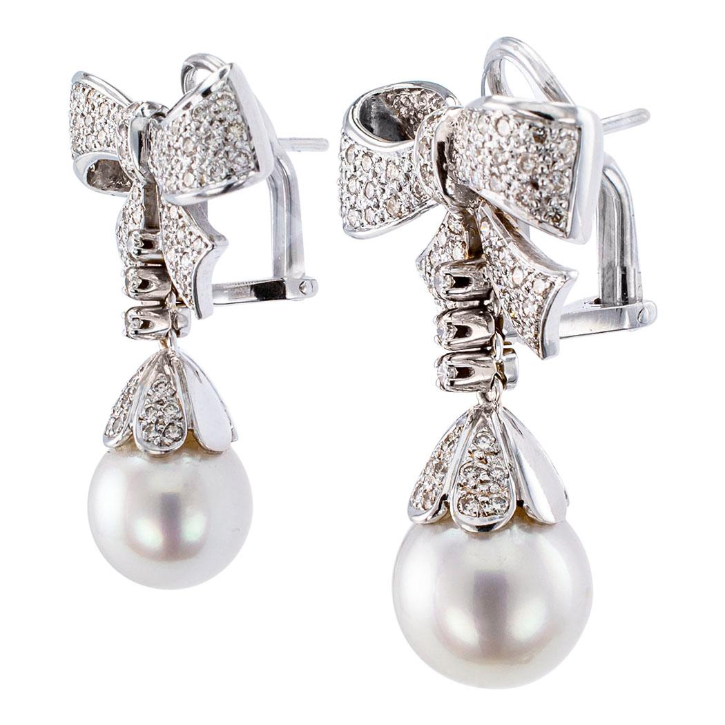 Diamond South Sea pearls and gold drop earrings circa 1970. The articulated designs feature a pair of diamond-capped South Sea pearls measuring approximately 12 mm, connected to bow-shaped motifs entirely pavé-set with additional diamonds, all
