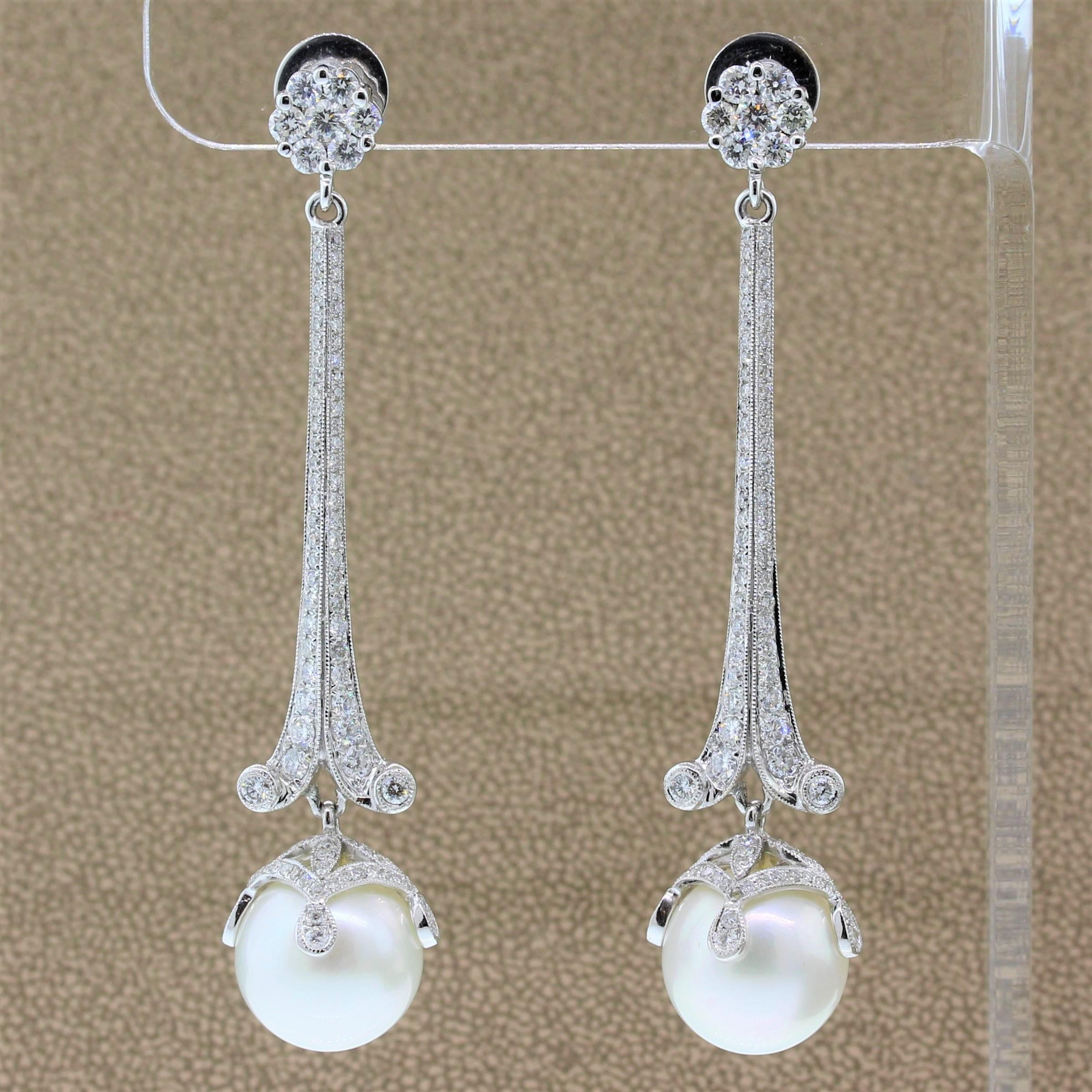 A striking pair of drop earrings featuring lustrous 12.5mm to 13mm South Sea pearls at the end of a long drop. The 18K white gold setting is studded with 2.76 carats of round cut colorless diamonds with a flower cluster at the post backing.