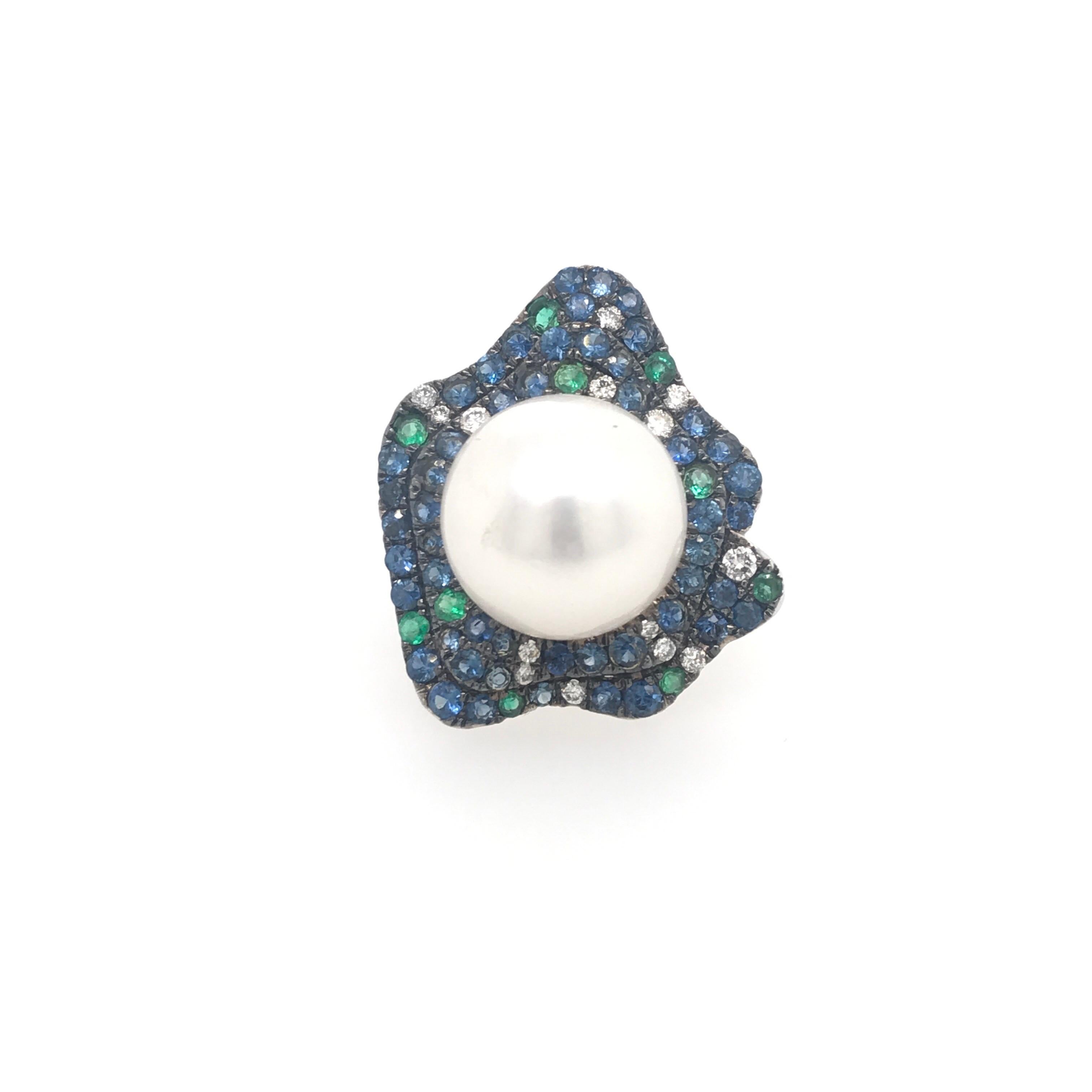 18K White Gold fashion ring featuring one South Sea Pearl measuring 13-14 mm flanked with diamonds, 0.21 carats, blue sapphires, 1.80 carats, and green emeralds 0.30 carats. 