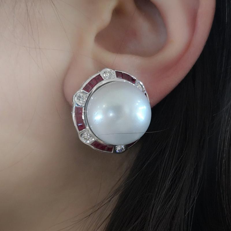 A pair of South Sea pearl and diamond earrings, with central 18mm South Sea pearls, surrounded by rubies and diamonds, in a repeating pattern of three calibré cut rubies and a round brilliant-cut diamond, mounted in 18ct white gold, with a folding