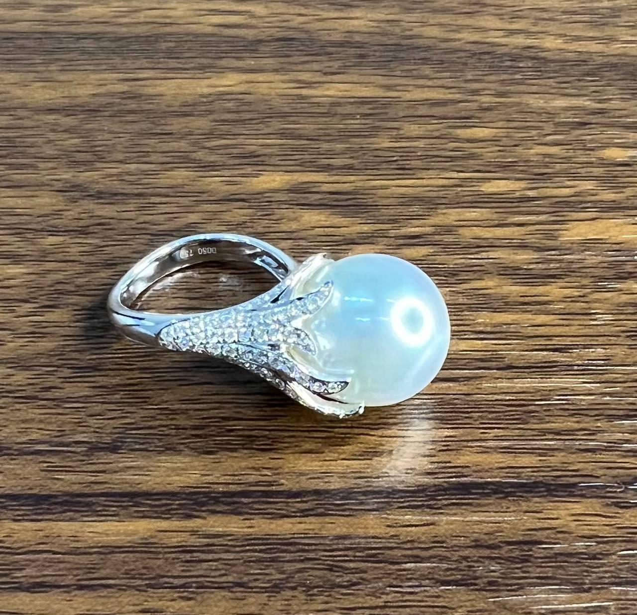A striking pearl and diamond ring. It features a large, lustrous south sea white pearl set at the center, surrounded by an intricate design of diamonds F/VS Quality. The diamonds are meticulously arranged in a claw-like setting, enhancing the
