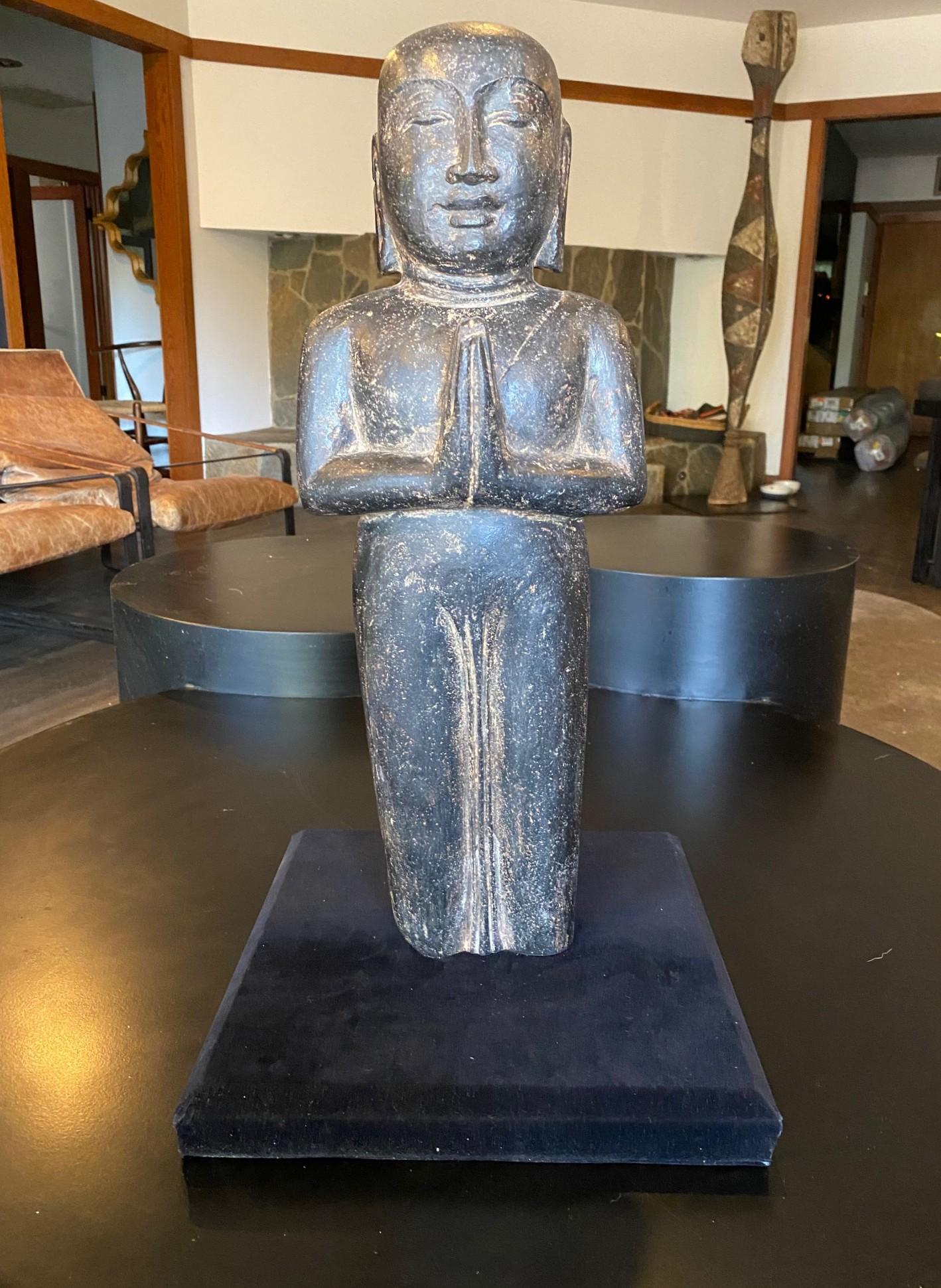 Una escultura/estatua de Buda sereno, alto, tallado en piedra, muy bello y llamativo, sobre un soporte de exposición personalizado.  

Creemos que este artefacto/fragmento de Buda es originario de Tailandia (cuando encontramos la estatua había una