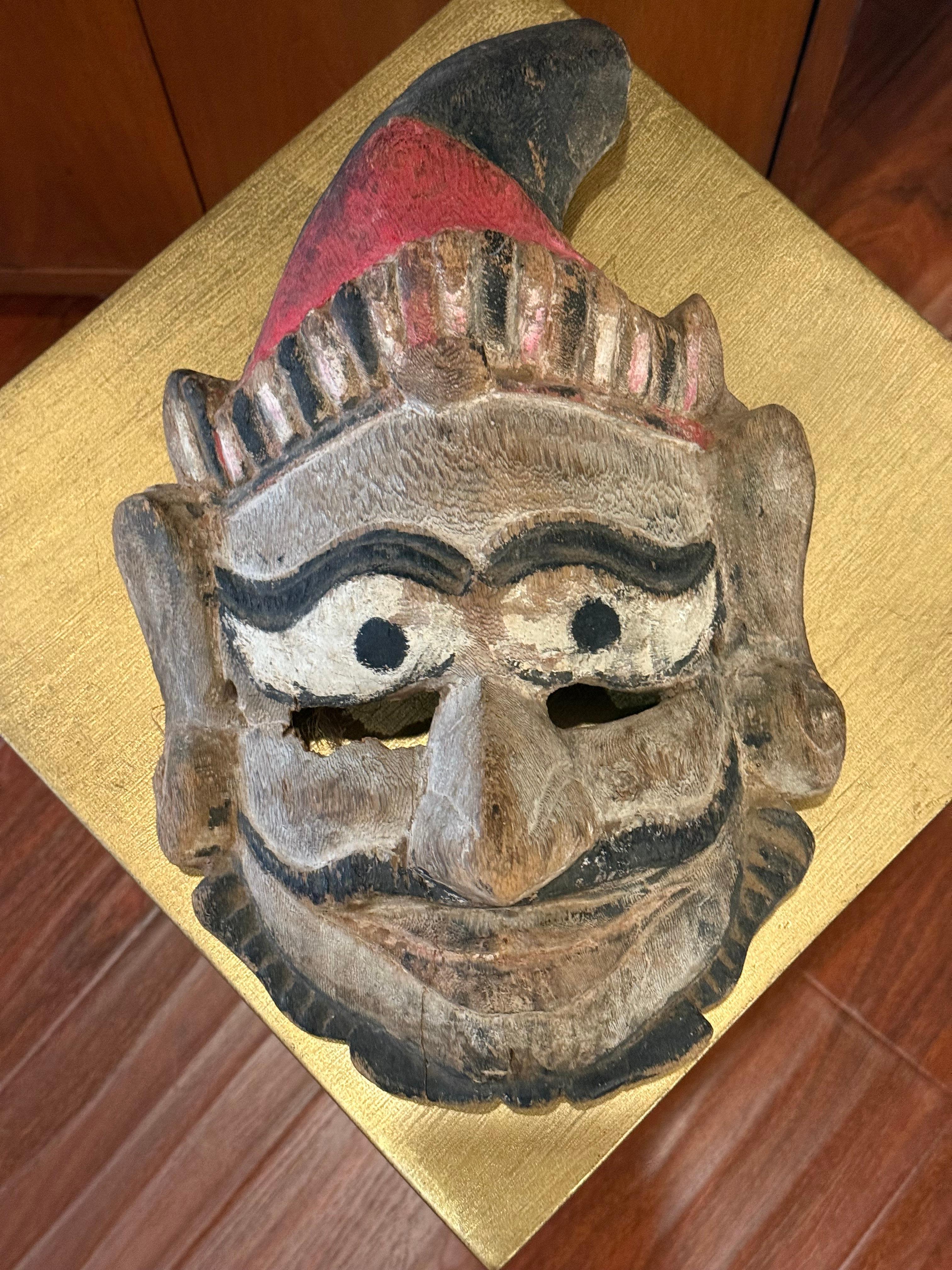An expressive tribal mask with pronounced brows, stylized features, and traces of red and black pigment, reflecting its ceremonial origins.

This hand-carved and painted wooden mask is likely a piece of ethnographic or folk art. Based on its style