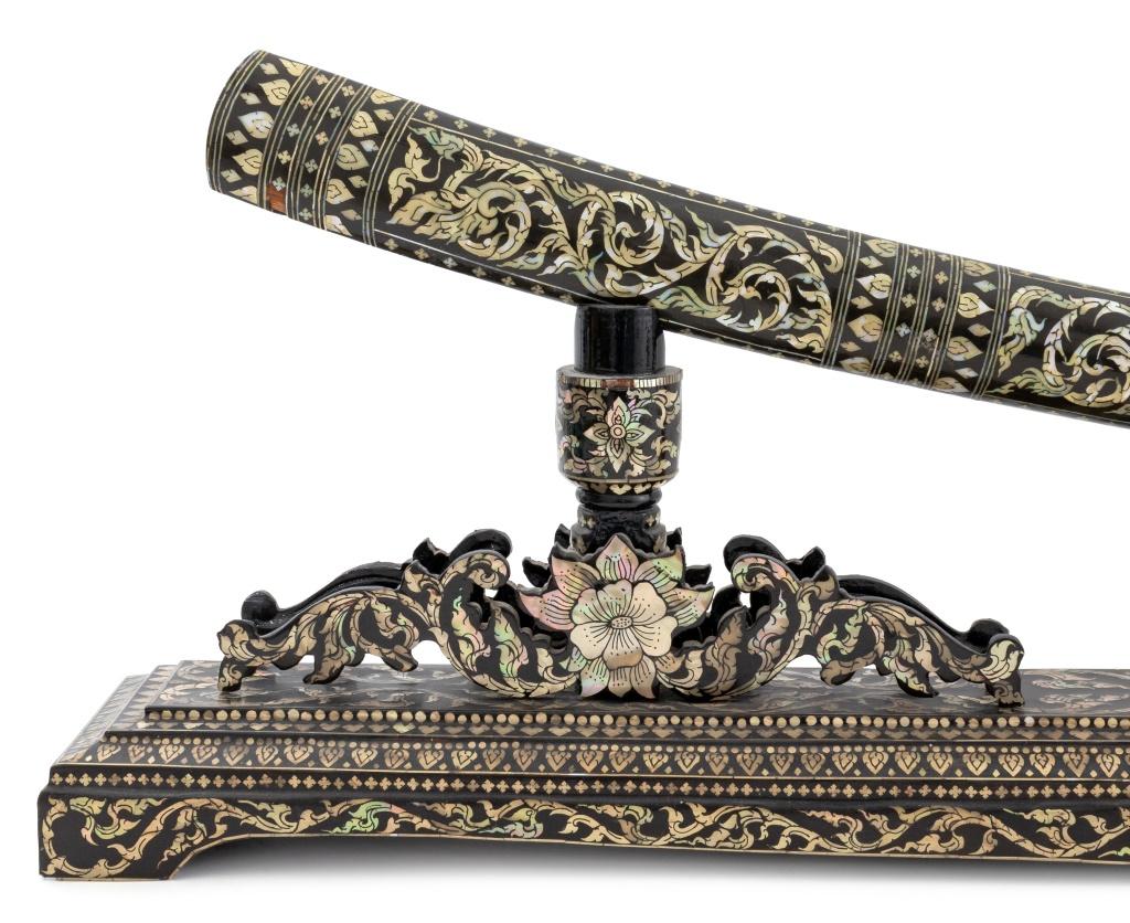 Épée Dha d'Asie du Sud-Est en laque noire incrustée de nacre, probablement thaïlandaise ou cambodgienne, début du XXe siècle, avec un fourreau orné sur un support d'épée avec des pieds en console et une décoration en forme de volute, la lame en