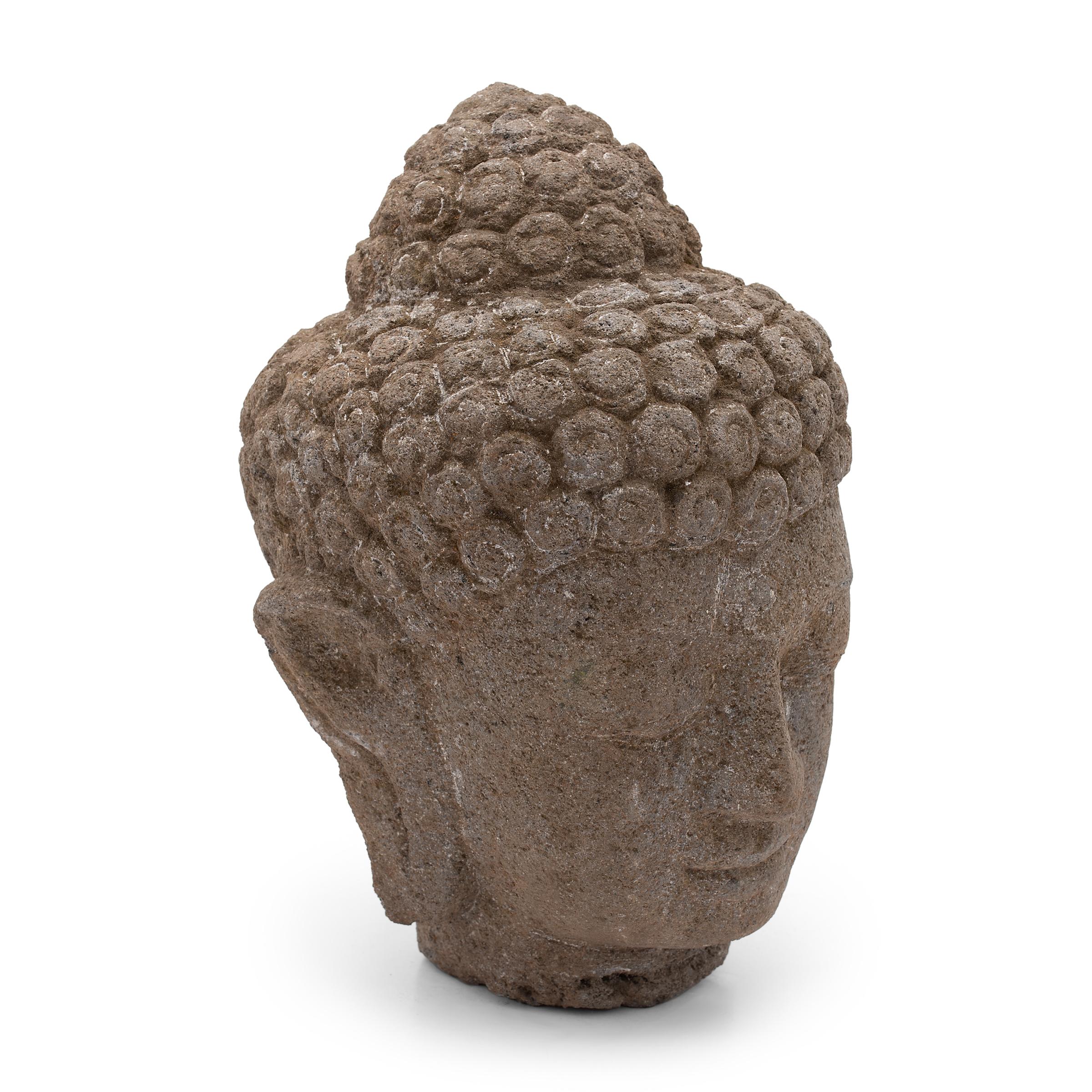 With closed eyes and a gentle expression, this large stone head depicts the Shakyamuni Buddha in calm meditation. Also known as Shaka, Gautama Buddha, or Prince Siddhartha, the historic Buddha Shakyamuni embodies virtues of wisdom and compassion and