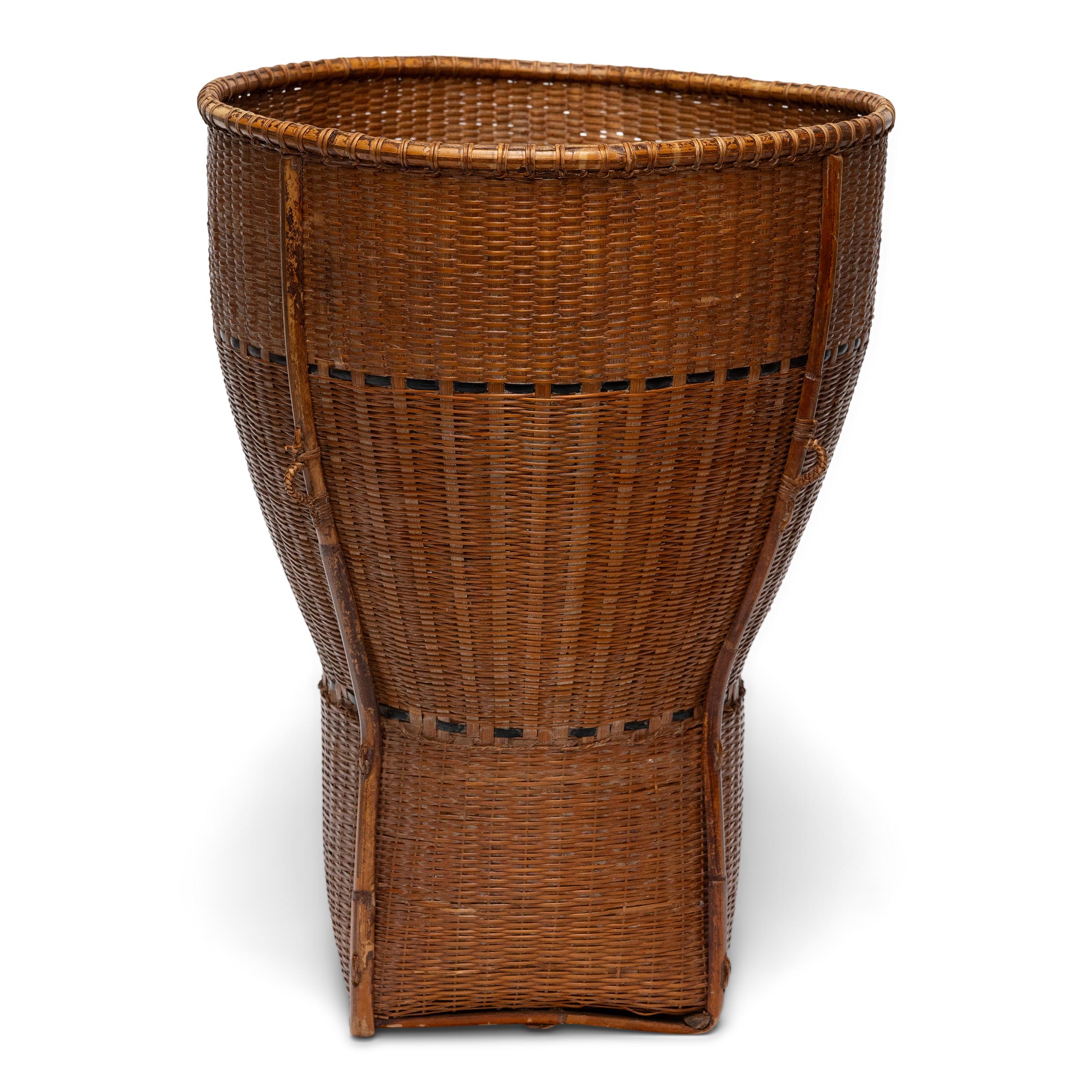 This hand-crafted storage basket is a vintage pack basket from southeast Asia, used in regions such as Thailand, Laos or Vietnam for harvesting crops or carrying personal belongings. The tall basket is woven with an elegantly tapered form, shaped