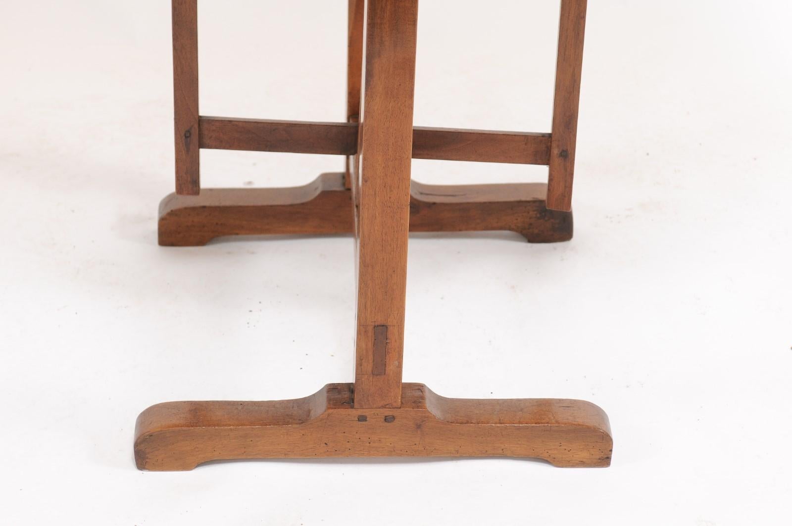 A rustic French solid walnut wine tasting table from the early 20th century, with round tilt-top and trestle base. Born in Southern France during the early years of the 20th century, this charming walnut wine tasting table features a circular