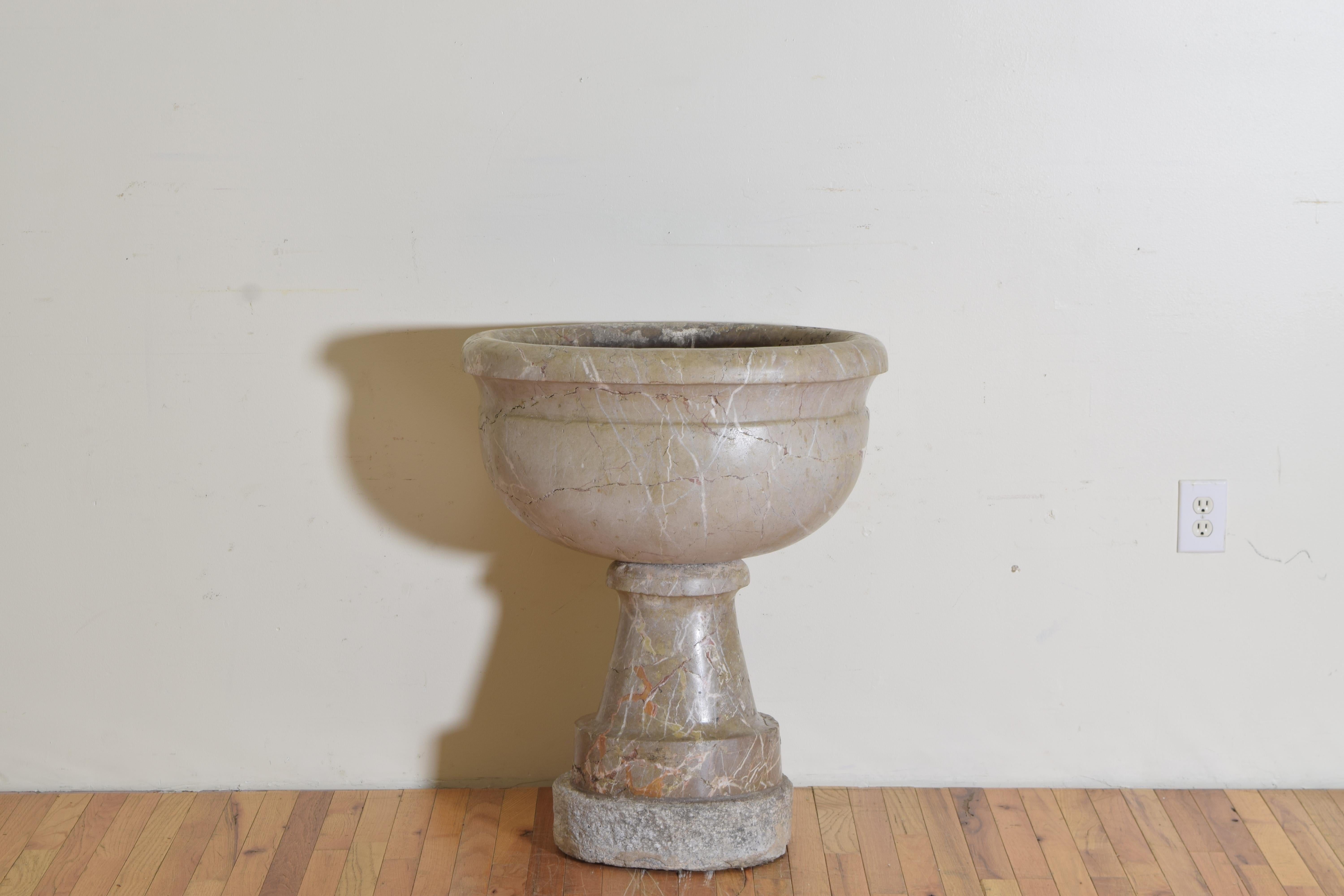 Of two piece construction, the bowl with rounded top edge and drain located at rear of bottom, the plinth form base raised on a cement slab, the rear of the base concave.