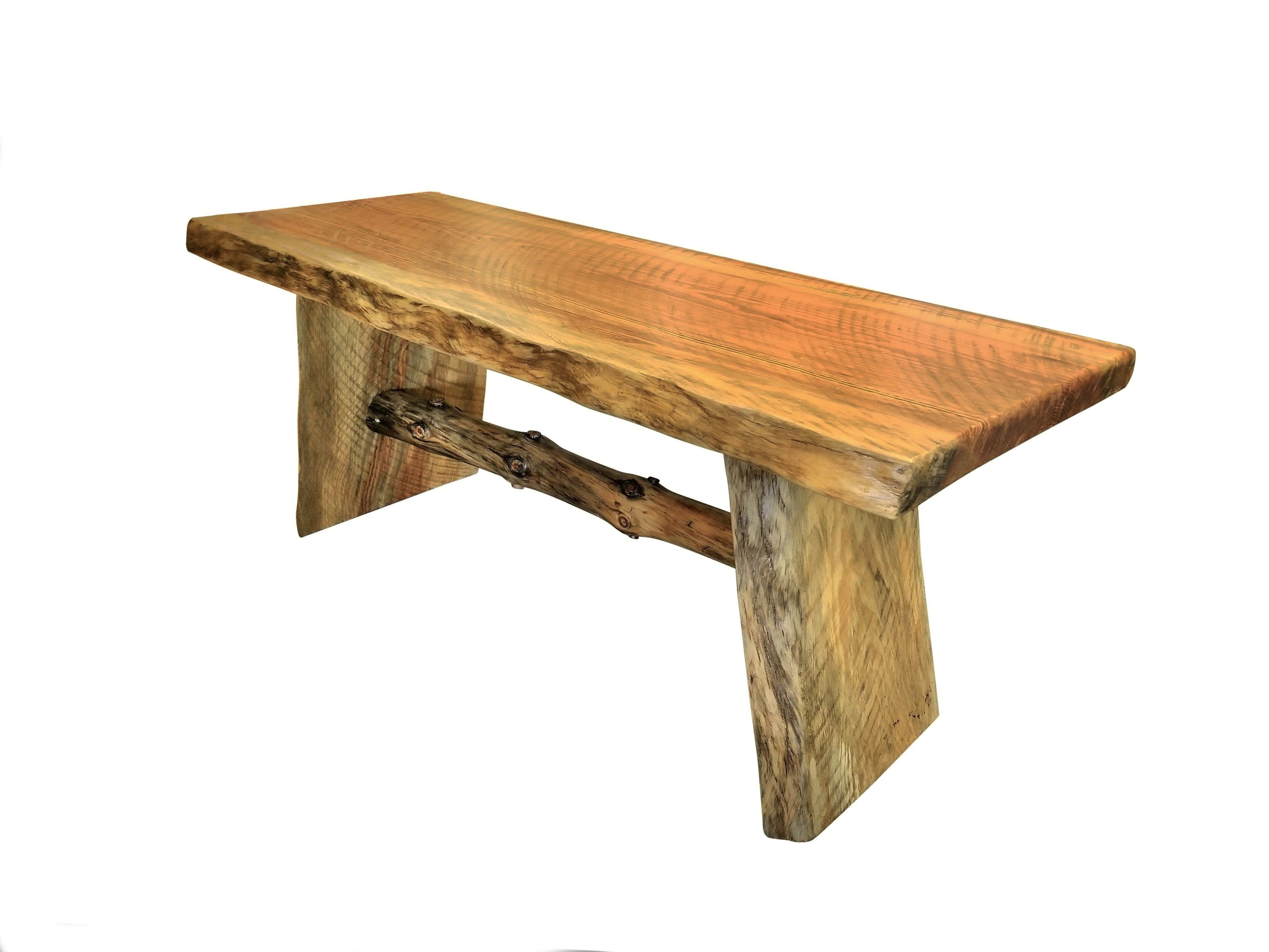 A rustic southern pine natural wood bench. Heavy, made with three pieces of solid plank wood with natural edging and richly grained throughout. Underneath a pine branch serves as a stretcher.