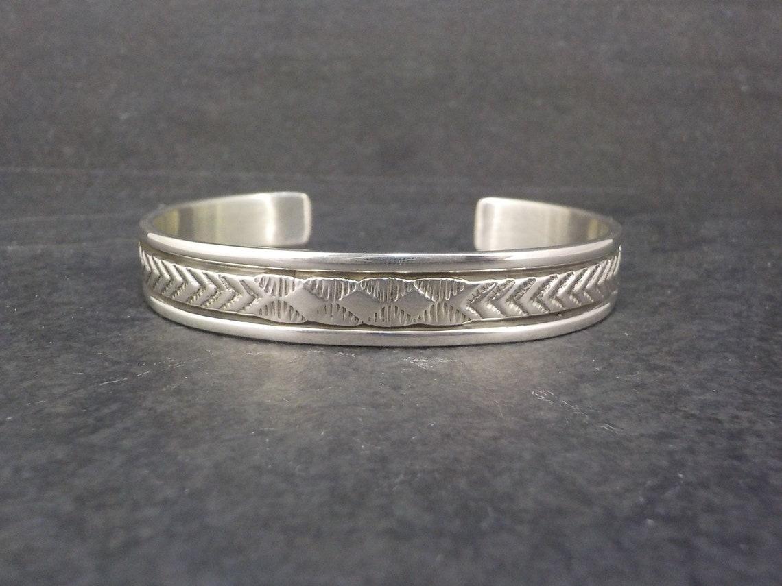 This beautiful Southwestern cuff bracelet is sterling silver.
It is a creation of Navajo silversmith Bruce Morgan.

Measurements: 3/8 of an inch wide - Inner circumference of 6 inches including the 1 inch gap.

Marks: B Morgan, Sterling

Condition: