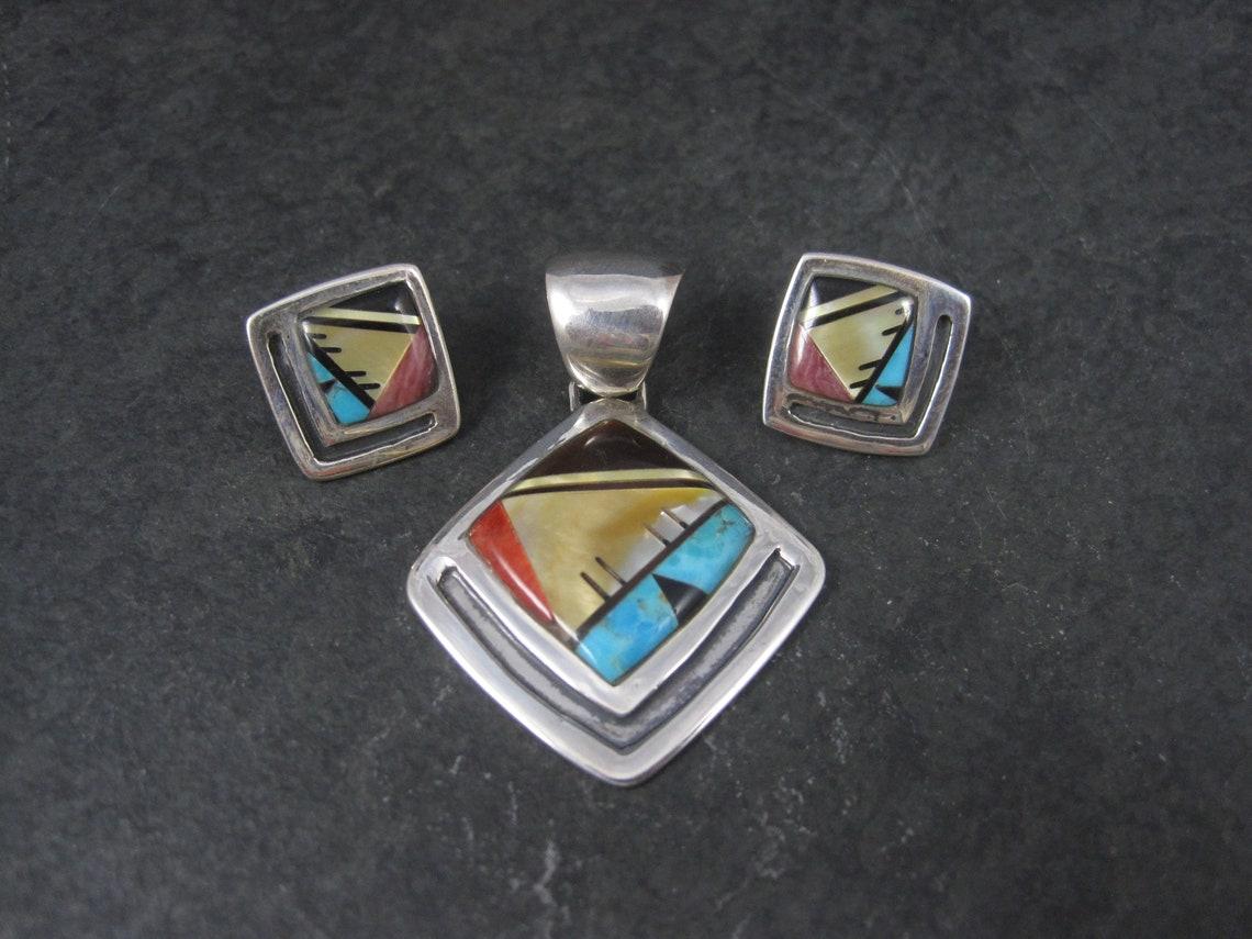 This gorgeous inlaid jewelry set is sterling silver.
It features turquoise, mother of pearl, coral and jet.

Earrings: 3/4 of an inch - 4.1 grams

Pendant: 1 1/4 by 1 3/4 inches

Marks: Sterling, YY

Condition: Excellent