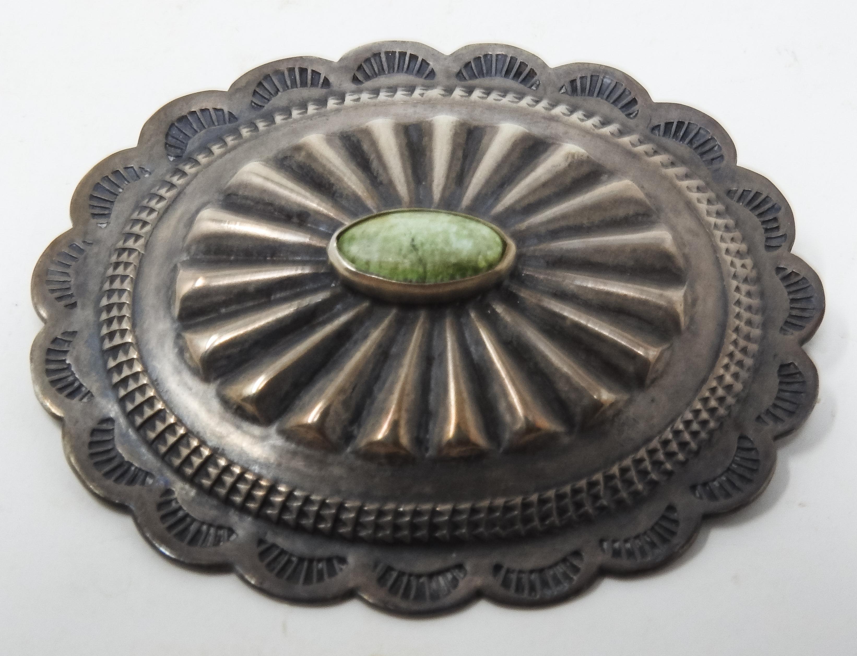 Offering this southwestern sterling silver and turquoise brooch. The brooch has a scalloped edge that has engravings in each of them. There is a band of geometric pattern going in towards the center. The closest to the center is raised being wider