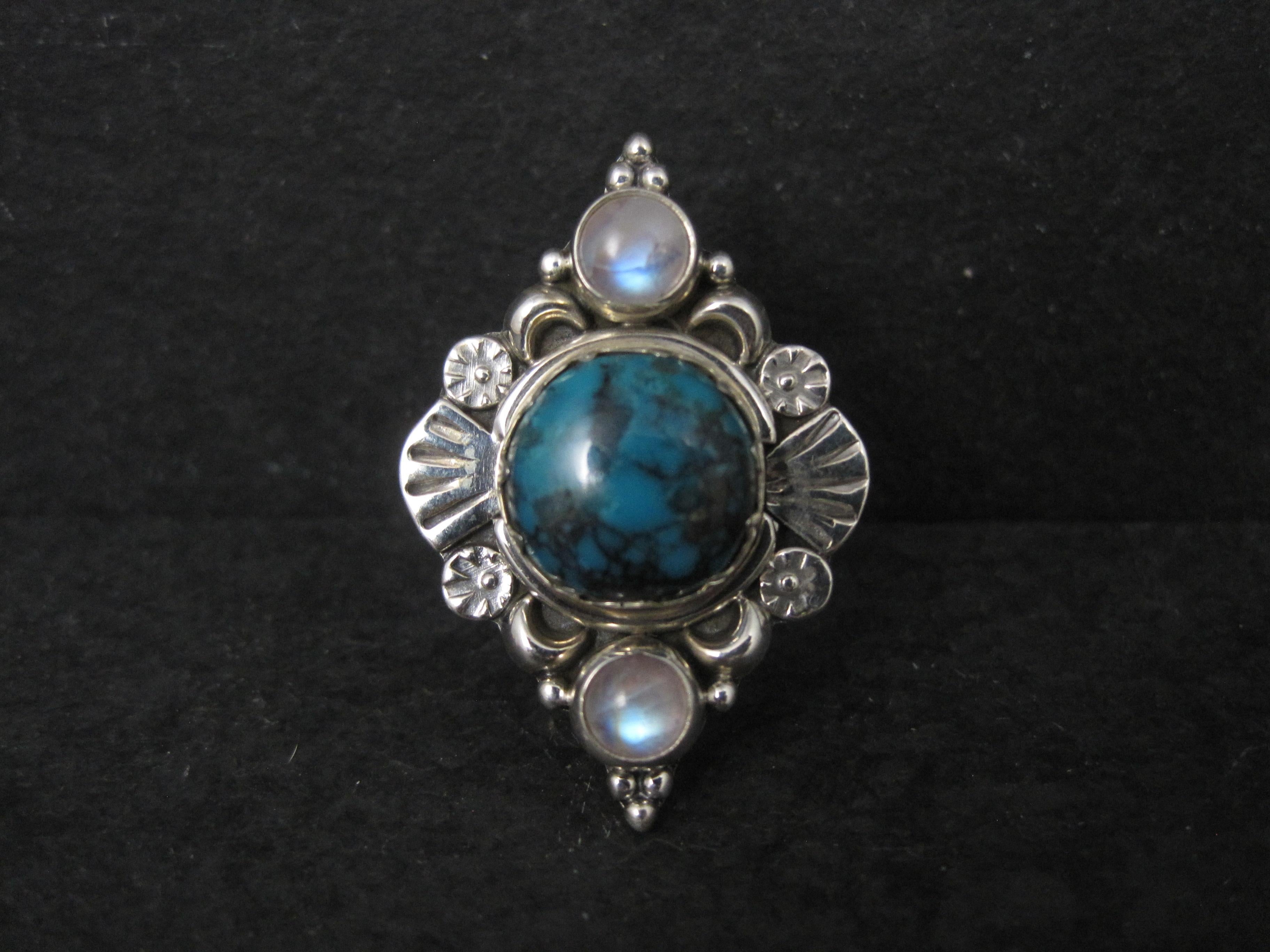 This gorgeous sterling silver estate ring features a Southwestern design.
It features a 12mm round turquoise accented by 2 round 5mm rainbow moonstones.
The face of this ring measures 7/8 of an inch east to west and 1 1/4 inches north to