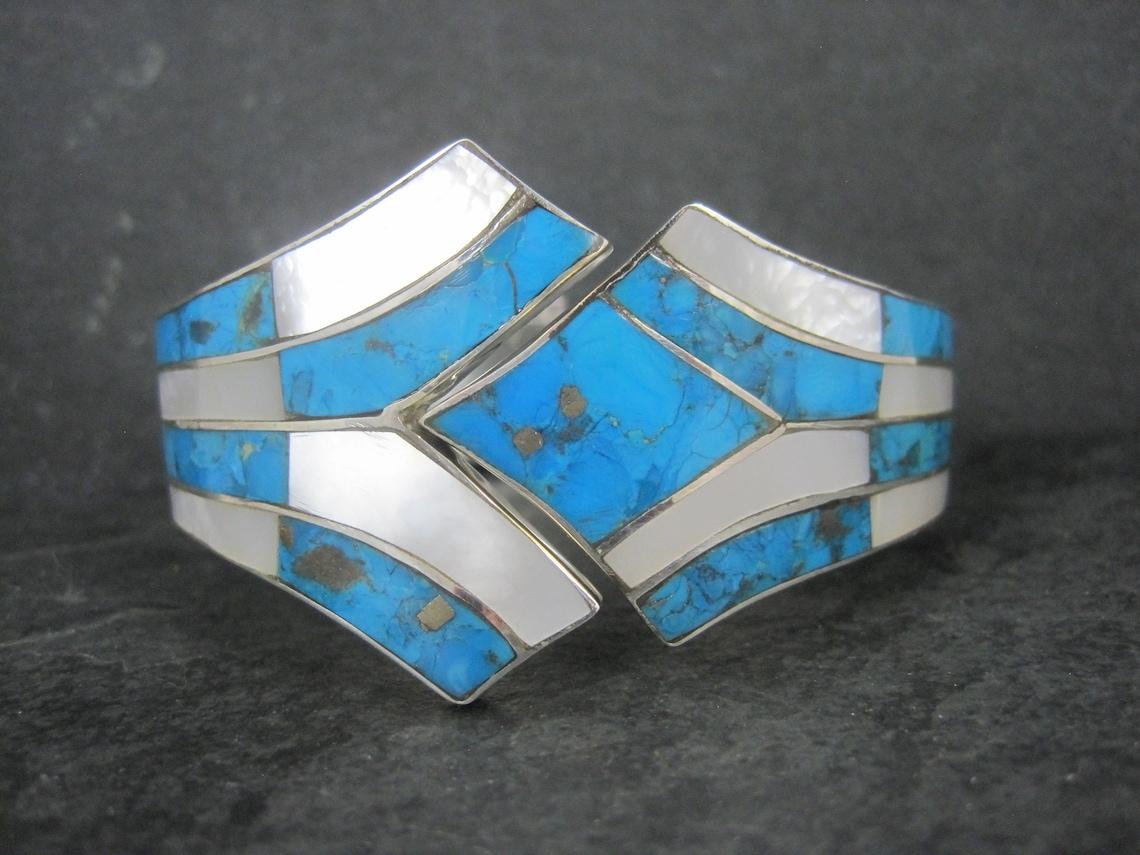 This gorgeous clamper bracelet is sterling silver.
It features a combination of mother of pearl and turquoise inlay with southwestern stampwork.

At the face this bracelet measures 1 7/16 inches wide and tapers down to 5/8 of an inch.
It has an