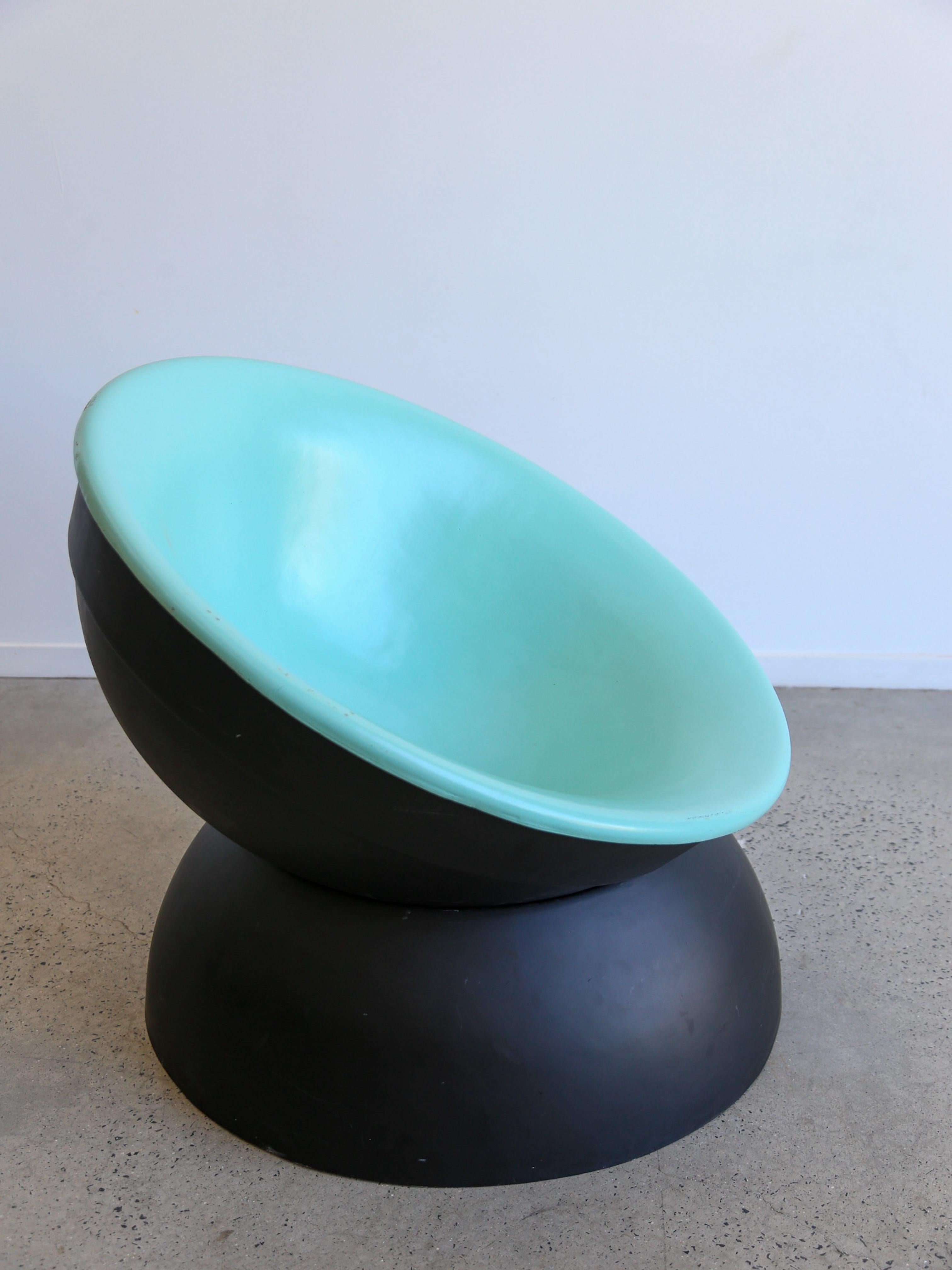 La chaise a une assise lisse, verte, en forme de bol, avec une finition mate, conçue pour le confort tout en conservant un aspect artistique et sculptural. La base est noire, large et arrondie, ce qui lui confère une grande stabilité tout en