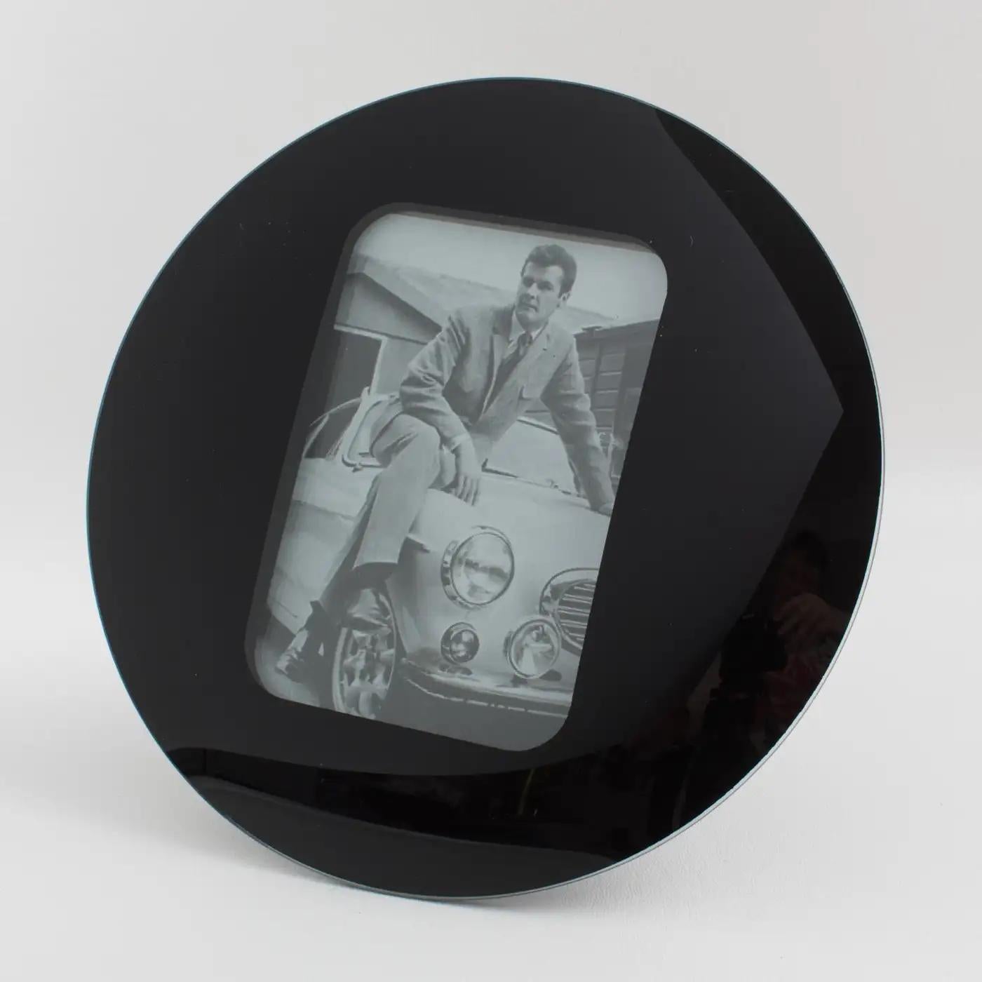 This lovely Space Age black glass picture photo frame was manufactured in the 1960s. The piece boasts a round domed design with a kinetic effect. The easel and back are covered with black suede paper. The picture photo frame can only be placed in a