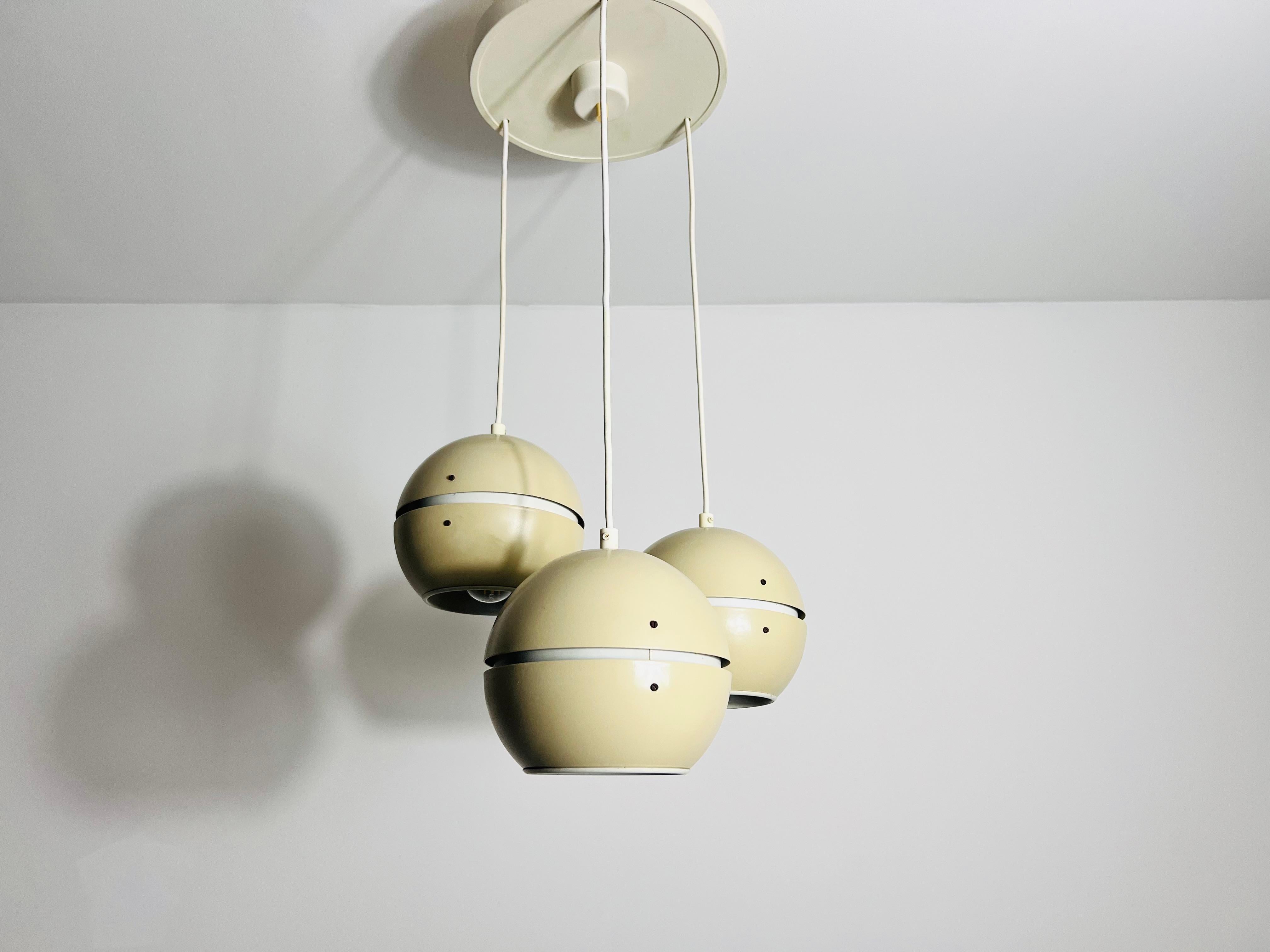 Questa lampada a sospensione a cascata degli anni '70, realizzata nell'ex DDR, incarna una sorprendente estetica moderna di metà secolo. Caratterizzato da tre paralumi in metallo sospesi da cavi elettrici, il design ricorda gli stili di