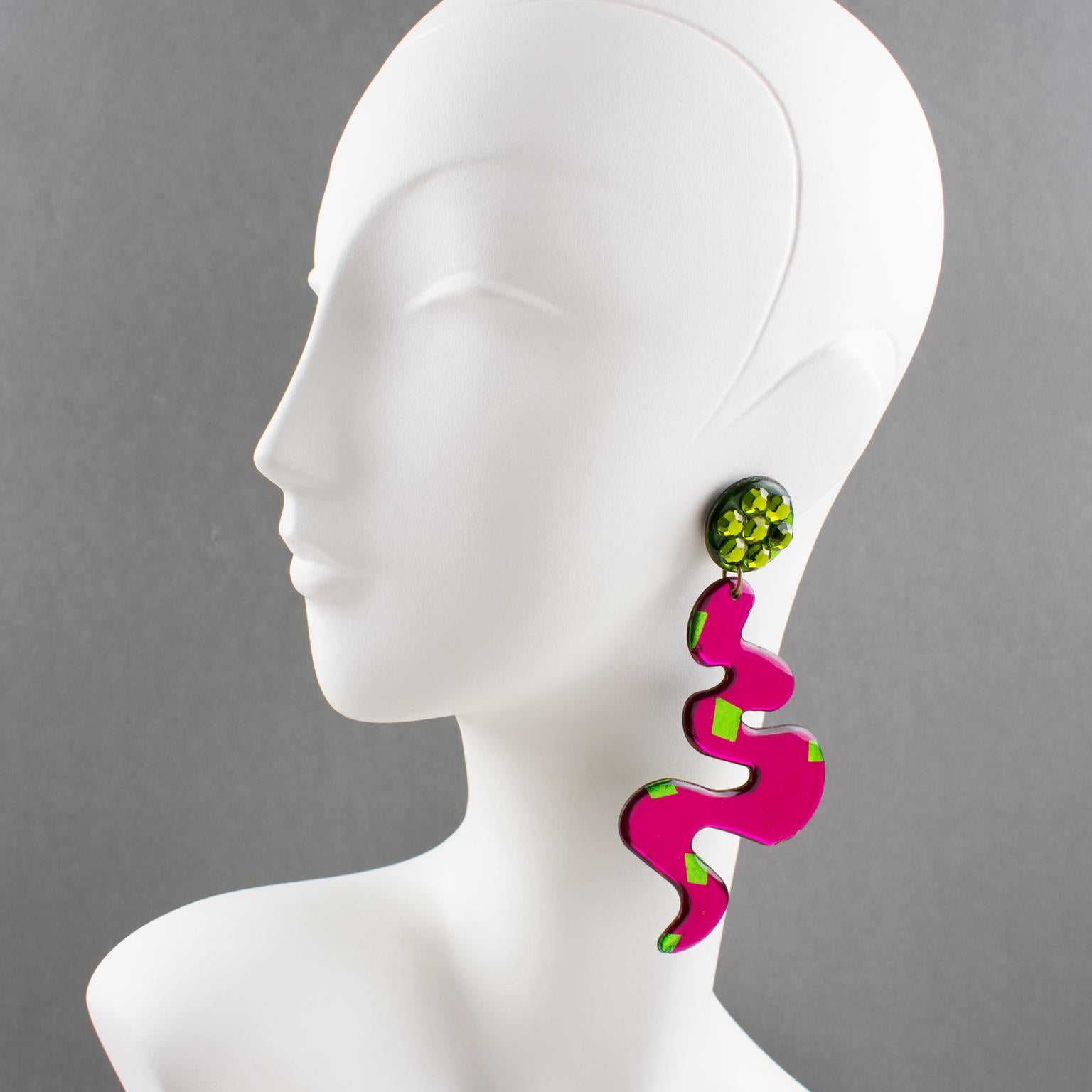 Handsome Italian Lucite or resin dangling clip-on earrings. Features an oversized chandelier shape with a freeform zig-zag design in hot pink and pistachio green colors. The colors have a mirrored textured pattern on a black background. Clip