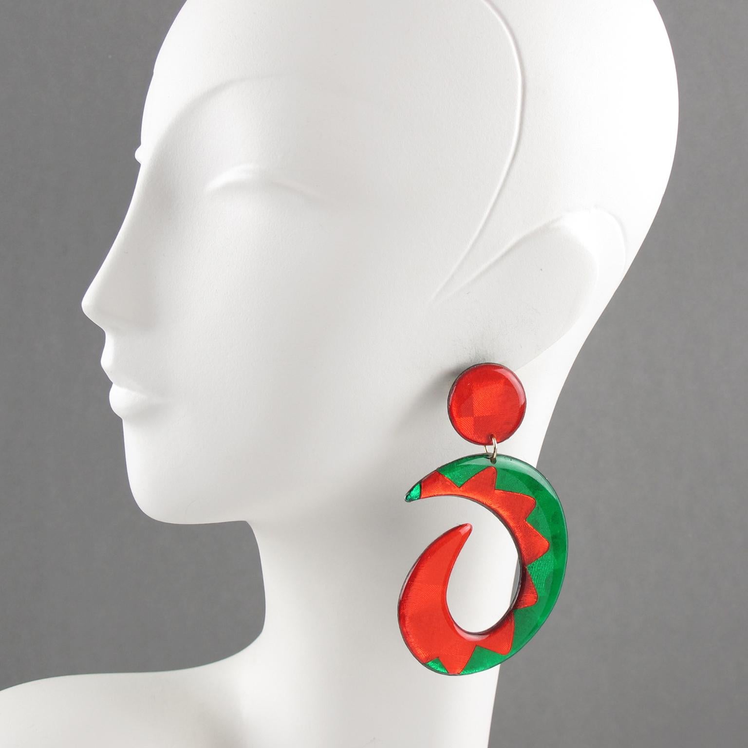 These impressive Lucite dangling pierced earrings boast an oversized chandelier shape with a free-form open hoop design in bright green and neon red colors with a glittering textured pattern and black background. These pieces are for pierced ears.