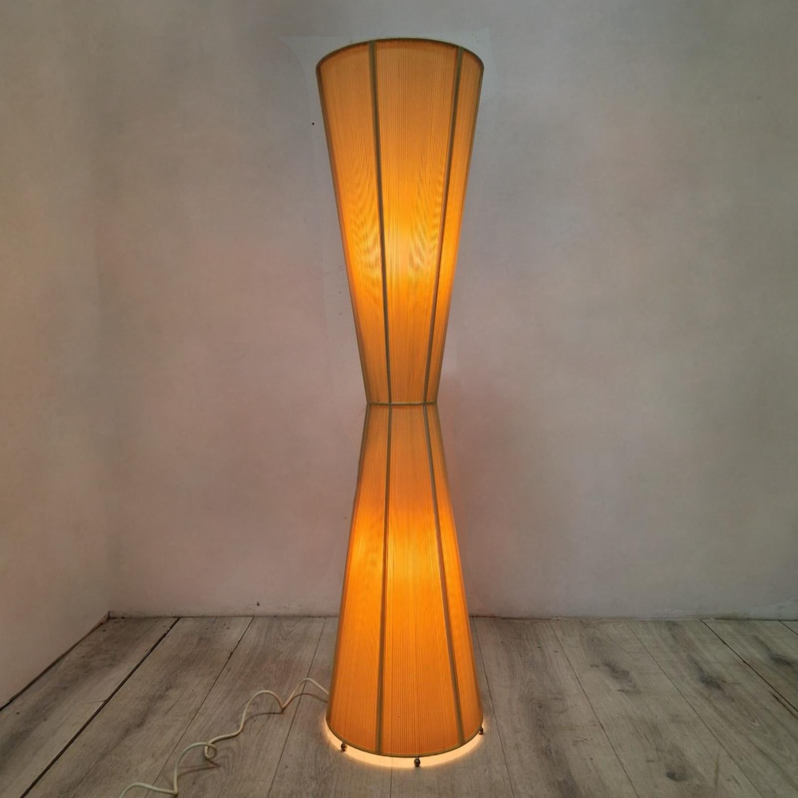 Large diabolo or hourglass shaped floor lamp. Skillfully made of metal wire with a plastic and thread shade.
Fitted with two E27 sockets. One for lighting the upper half and one for lighting the bottom half.
The lamp stands on small chromed metal