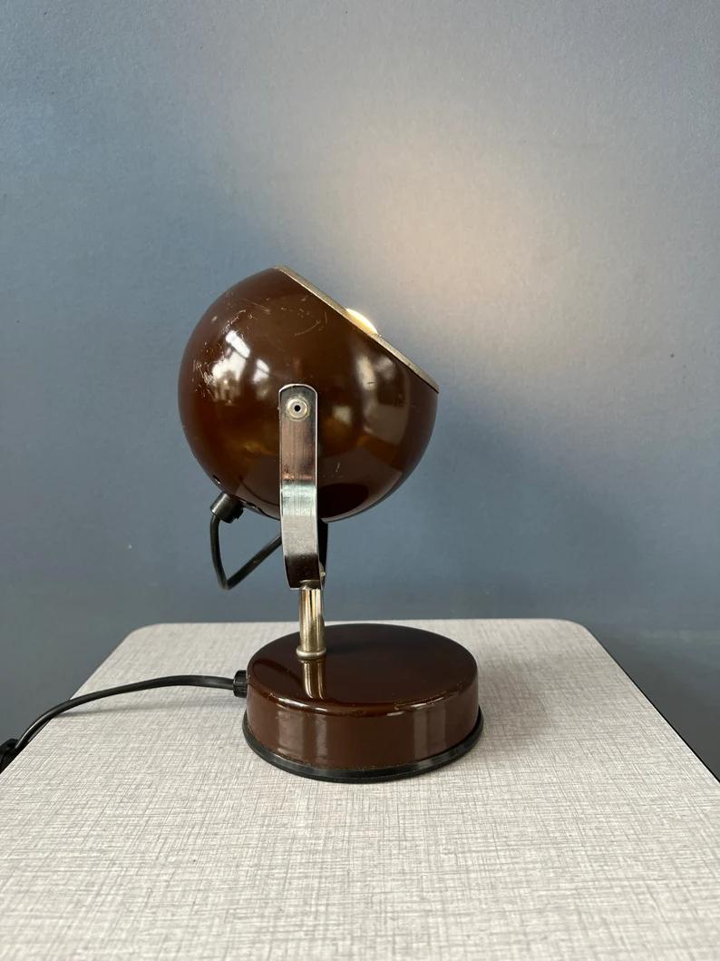 Small space age eyeball table lamp in brown colour. The eyeball shade can be turned in different directions. The lamp is made out of metal. The lamp requires one E14 lightbulb and currently has an EU plug (easily used outside EU with
