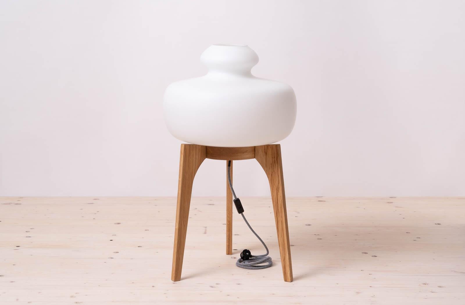 Questa lampada da terra degli anni '60 è stata realizzata dal produttore ceco ULUV (Ustredi Lidove a Umelecke Vyroby). Ha un grande paralume in vetro bianco latte montato su una base a treppiede in legno di Oak. Emette una luce calda e delicata che