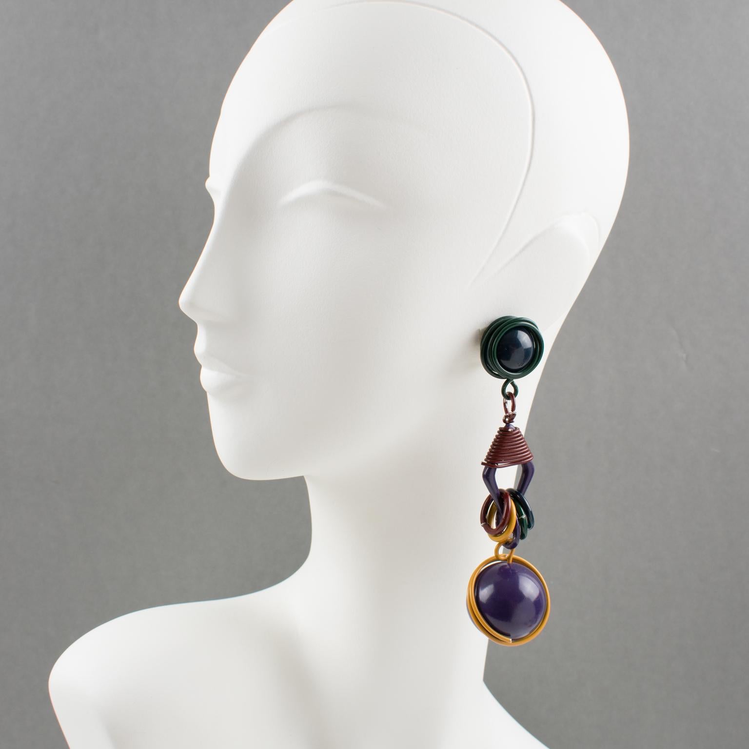These stunning futuristic dangling clip-on earrings feature a cool Space Age 1980s design, with shoulder duster dangle articulated wired elements complimented with rings and huge beads. The multicolor enameled metal has fall colors in purple,
