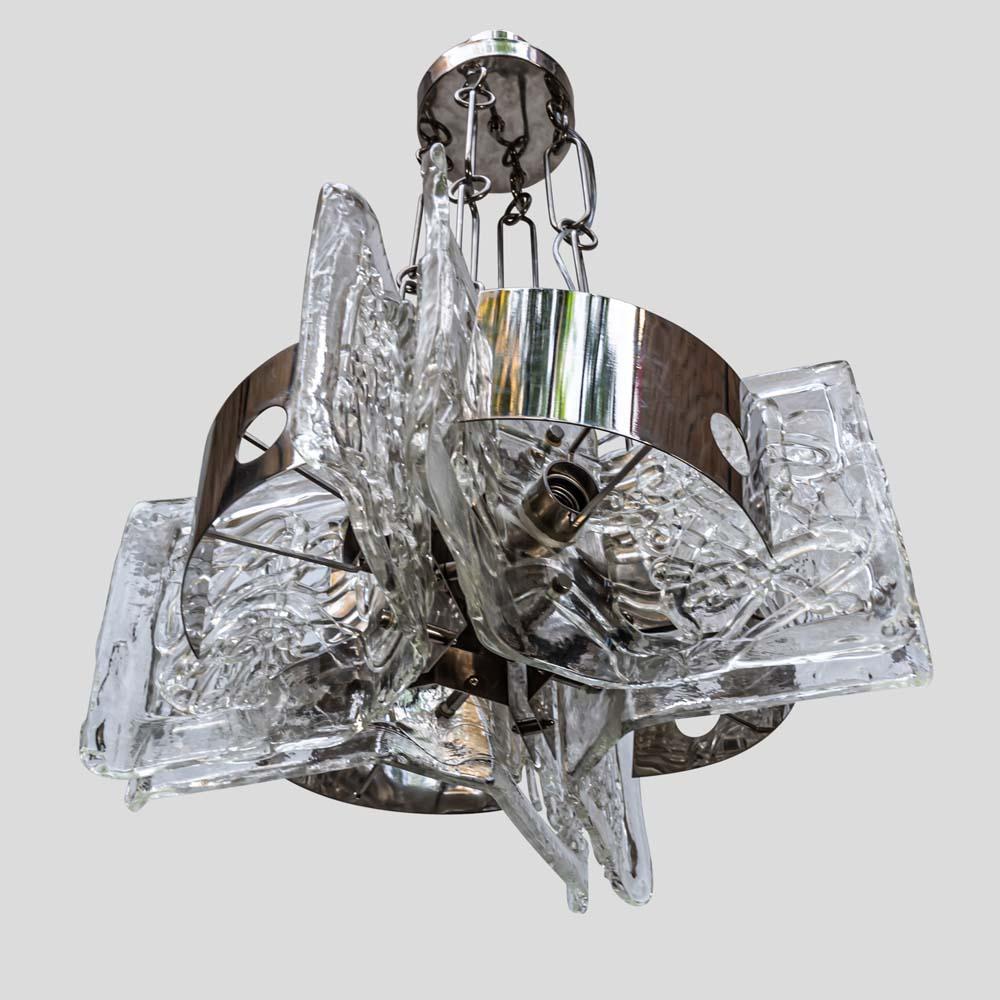 This is a 1970s space age ceiling light. This light features four angulated large glass sheets with spaghetti-like glass decoration with curved chrome metal shades which covers the light bulbs to creates a lovely defuser. The structure is held by
