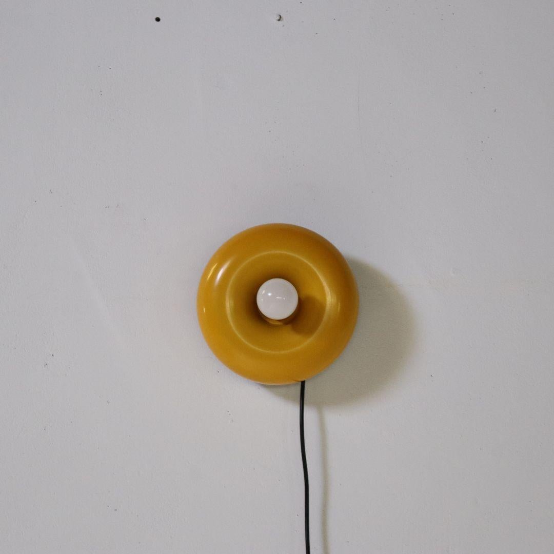 Eine sehr schöne Wand-/Tischleuchte, entworfen von Ingo Maurer, Deutschland 1966. Die Lampe hat die Form eines Donuts und der gelb lackierte Schirm ist in der Höhe verstellbar. Die Lampe lässt sich leicht an die Wand hängen, kann aber auch als