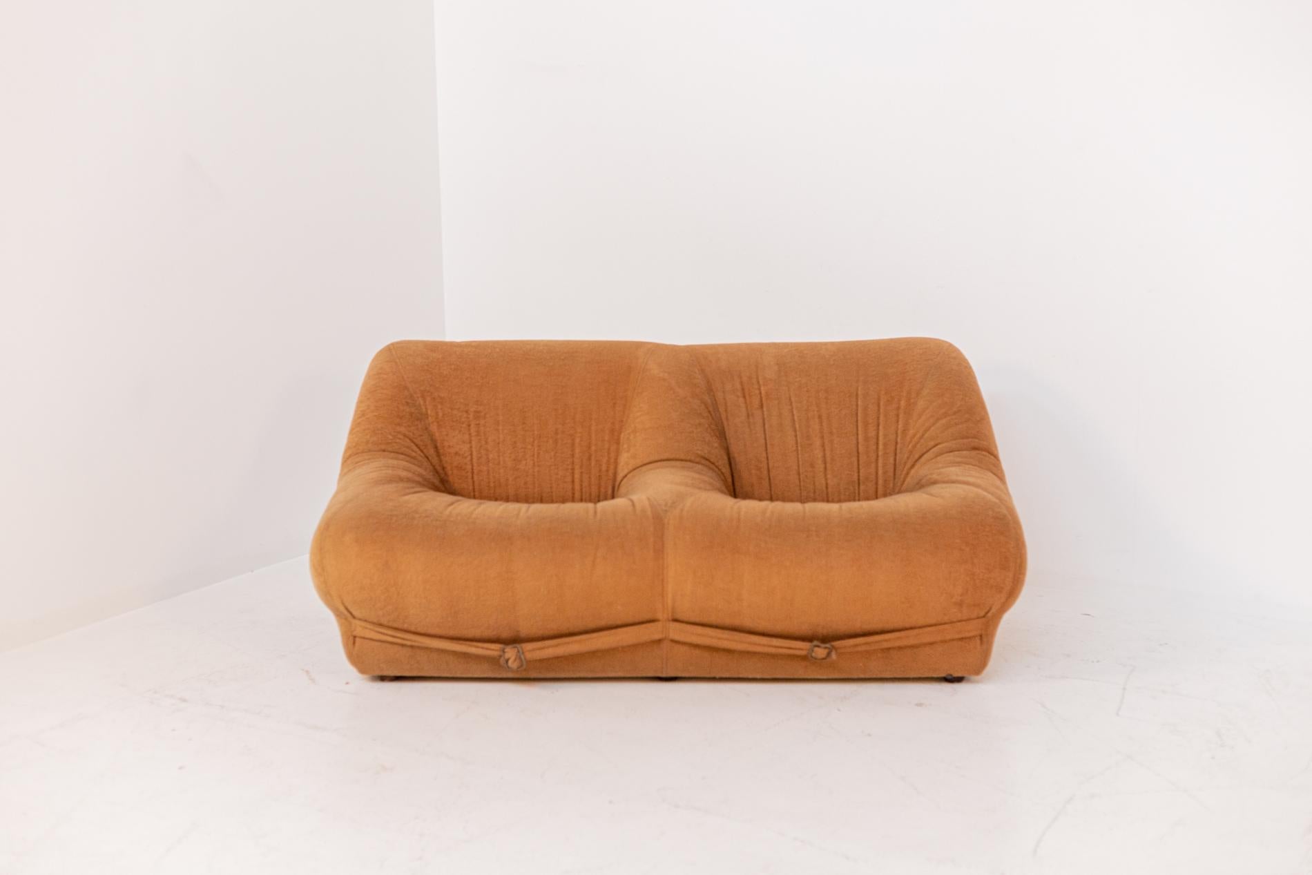 Beautiful two seater Italian velvet sofa from the Space Age period of the 70s.
The Italian sofa was made of dark orange velvet fabric. Its lines are very rounded with soft and enveloping shapes. 
In the back and under the feet we find a belt also