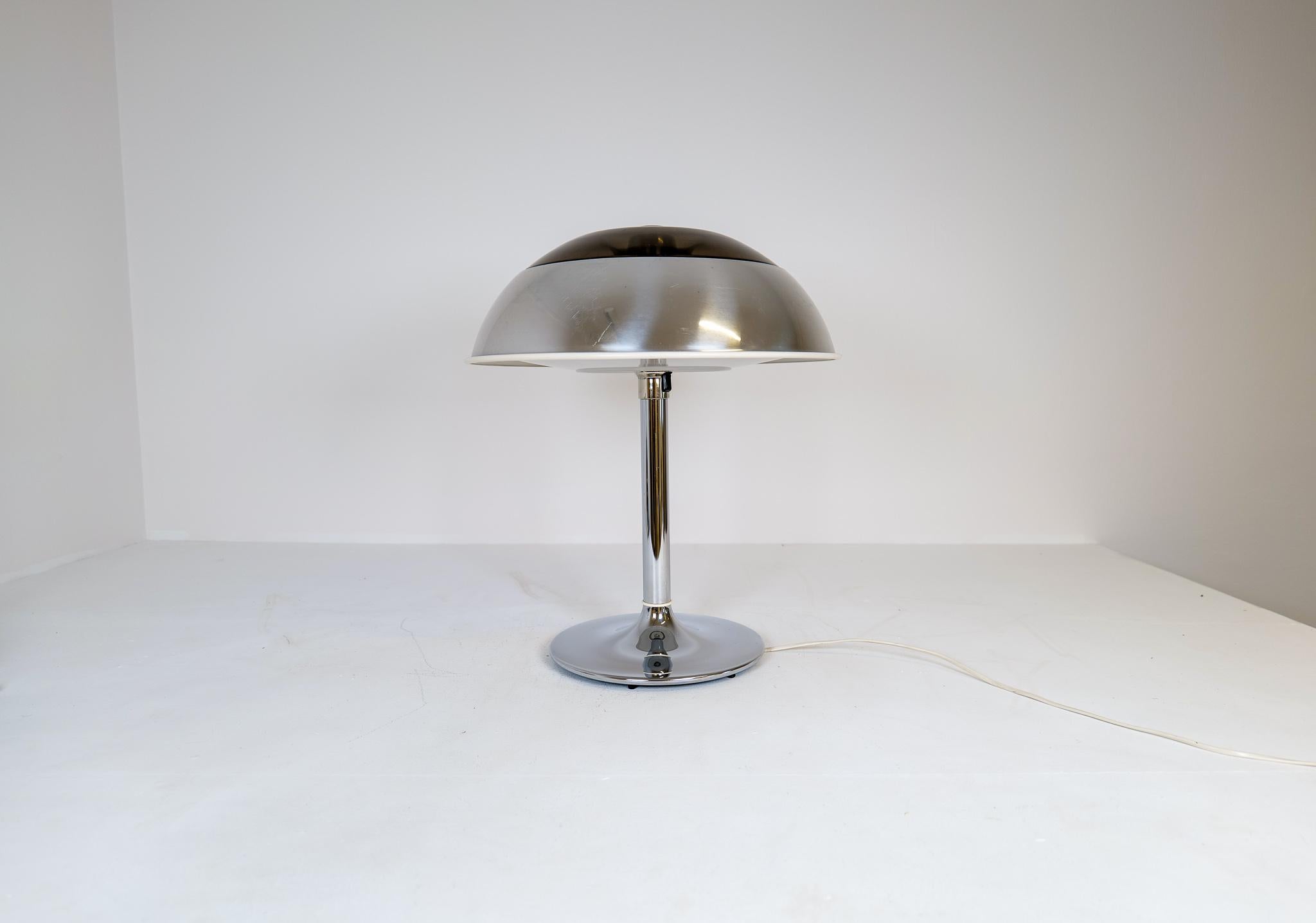 Diese große, verchromte Tischleuchte wurde in den 1970er Jahren bei Fagerhults Belysning in Schweden hergestellt.
Der Schirm ist aus verchromtem Metall und Kunststoff, der Rest aus verchromtem Metall. Wenn sie angezündet wird, gibt sie ein schönes