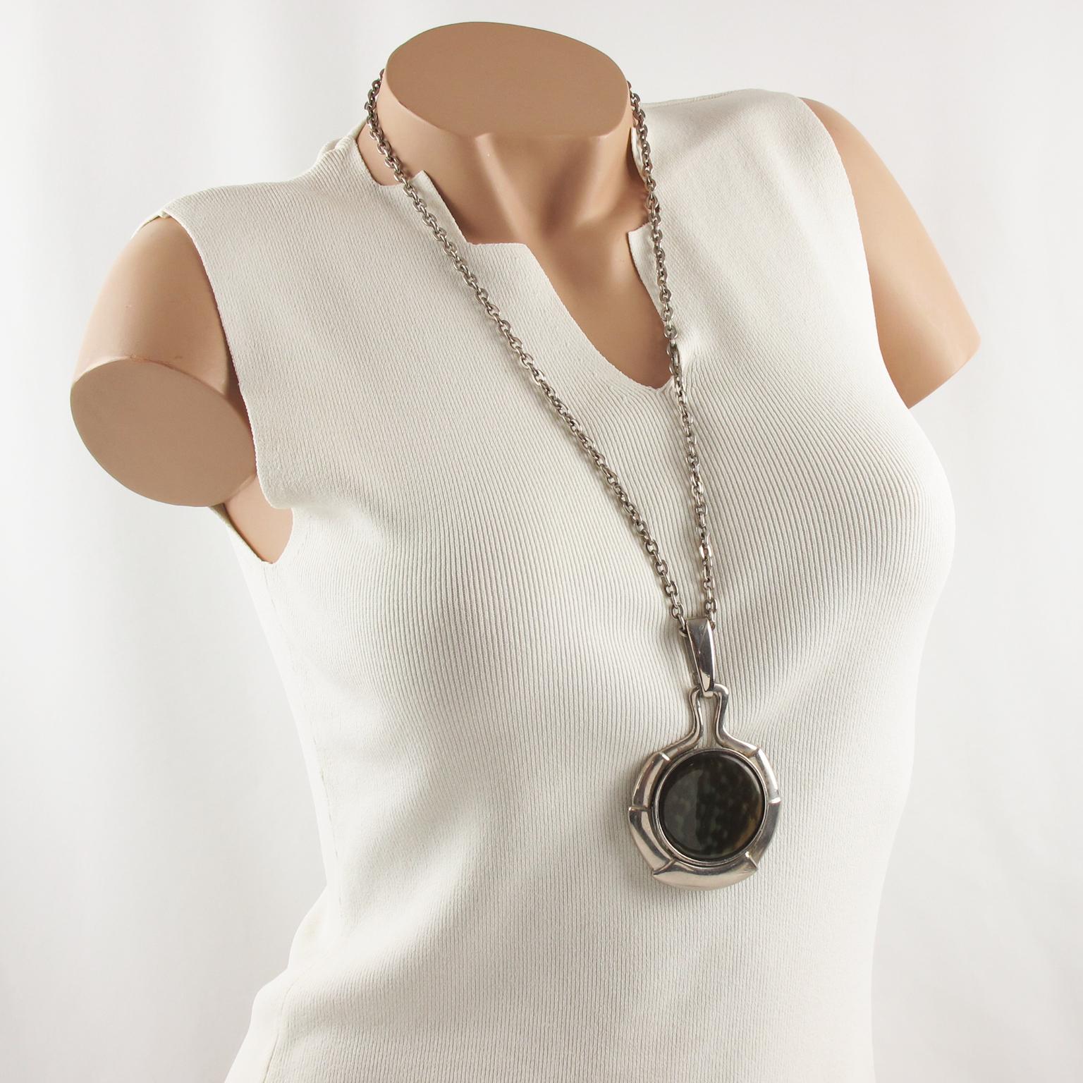 This lovely Space Age Mid-Century modernist pendant necklace features a heavy silvered metal extra-long chain complemented with an oversized silvered metal disk pendant. The pendant is topped with a large resin flat cabochon in iridescent green and