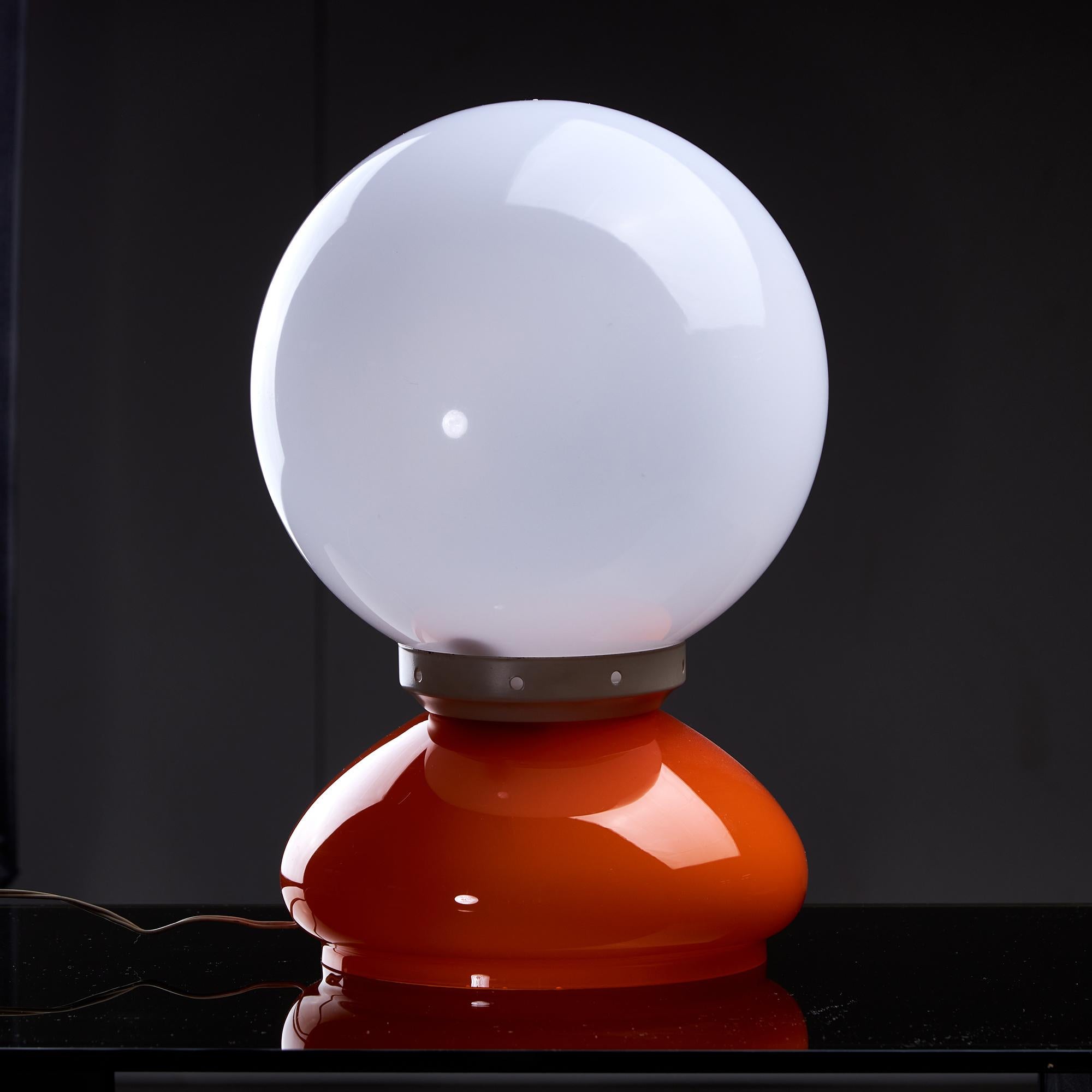 Voici la charmante lampe à poser de l'âge de l'espace qui capture l'esprit des années 1970. Son design se caractérise par une sphère en verre orange aplatie en guise de base, surmontée d'un abat-jour en plastique blanc. Une ceinture en métal relie