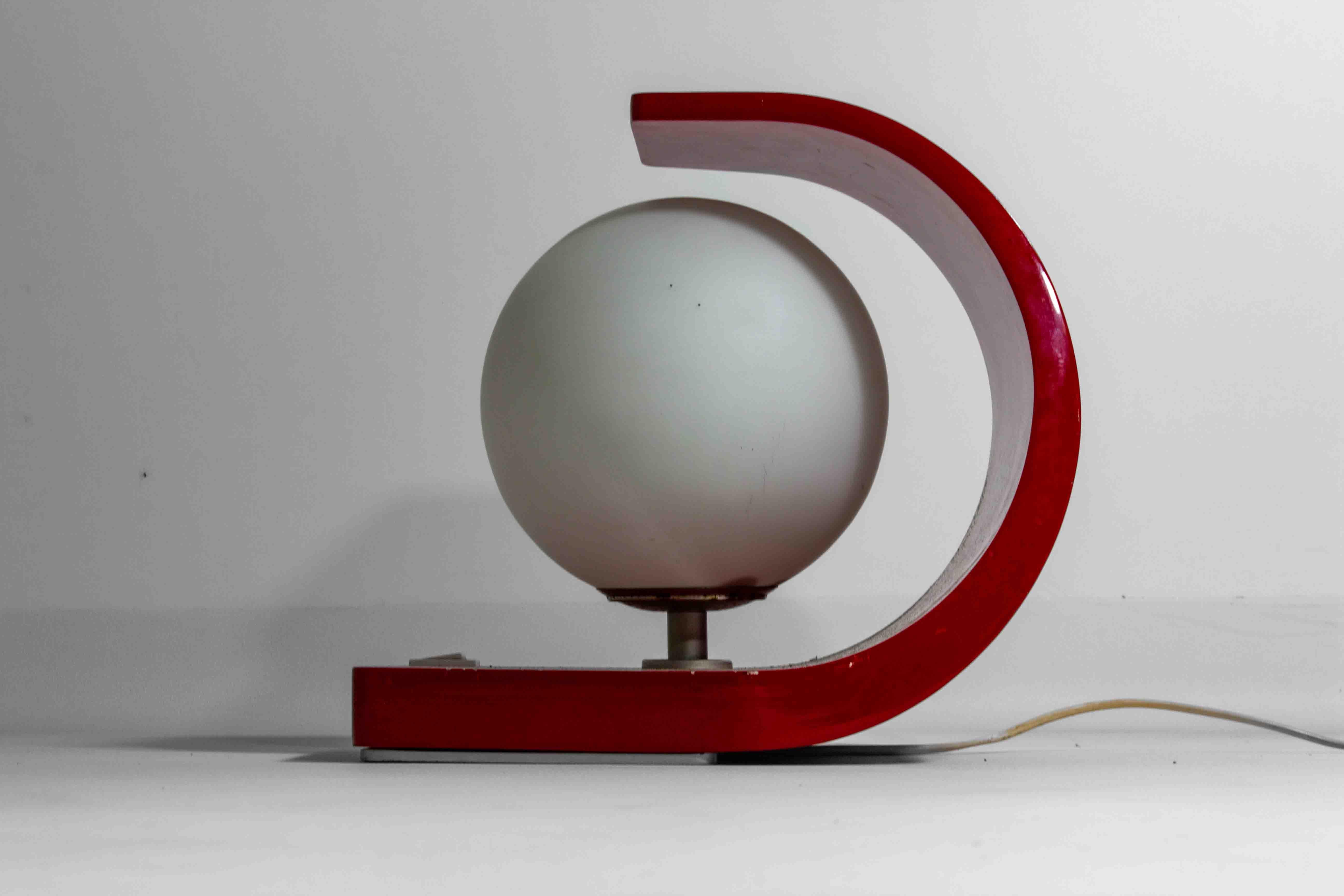 Cette lampe orbe de l'ère spatiale des années 1960 se distingue par sa base rouge à capuchon et son abat-jour sphérique en verre au lait, incarnant l'esthétique du design futuriste de l'époque. La lampe est dotée d'une base incurvée en émail rouge