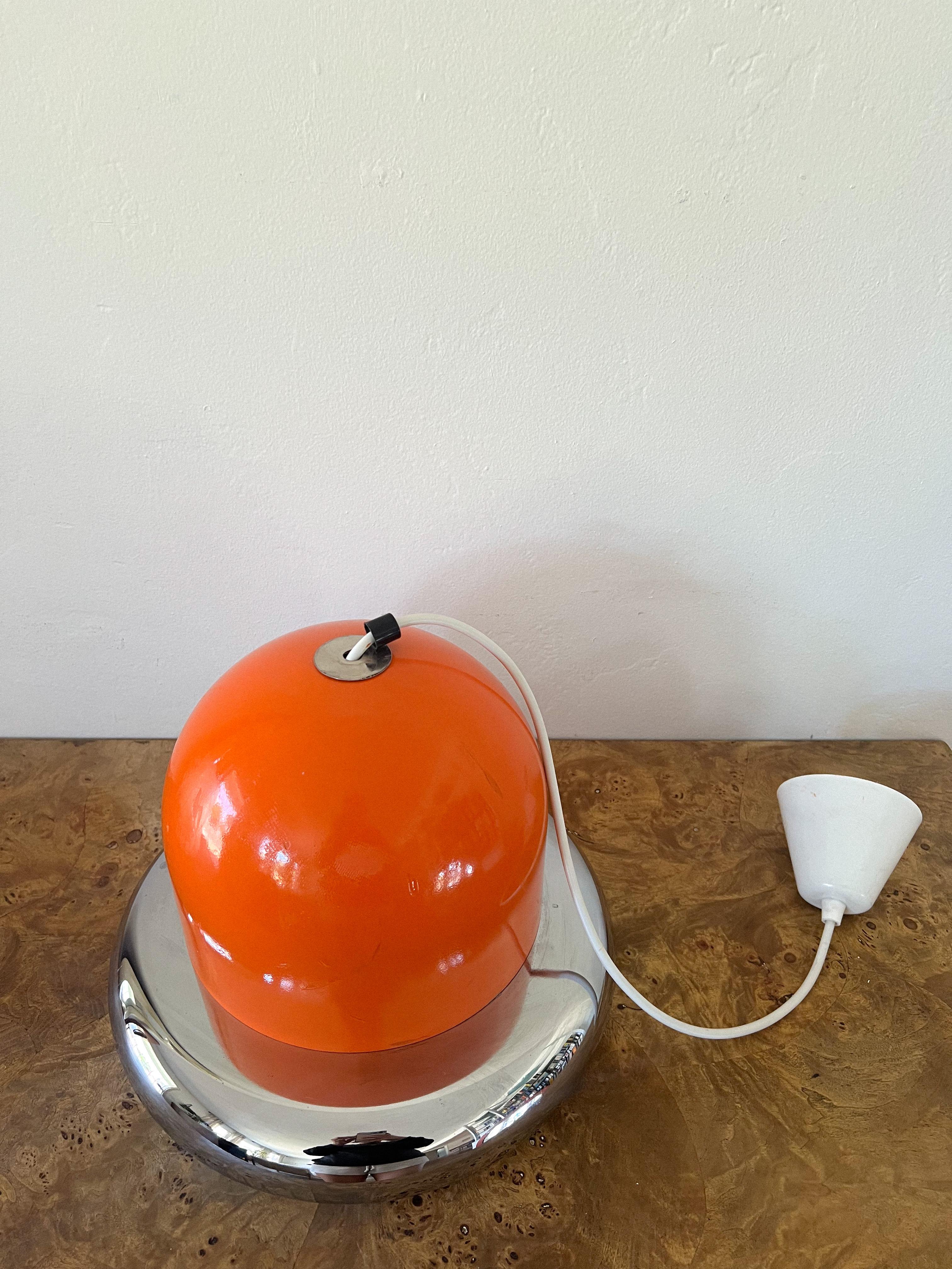 La suspension de l'ère spatiale attribuée à Guzzini présente un abat-jour orange associé à un cadre élégant en aluminium ou en métal. Cet abat-jour distinctif émet une magnifique lueur qui se reflète sur la pièce chromée qui se trouve en dessous.