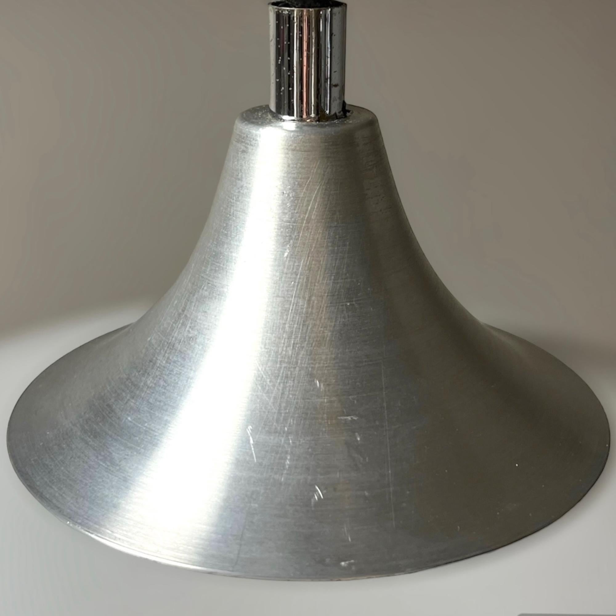 Iconica lampada spaziale degli anni '70 realizzata da Stilux Milano. Questa lampada è composta da un piano conico in metallo argentato che sostiene un grande paralume curvo in polimetacrilato bianco.  

Il meccanismo di chiusura è il famoso 