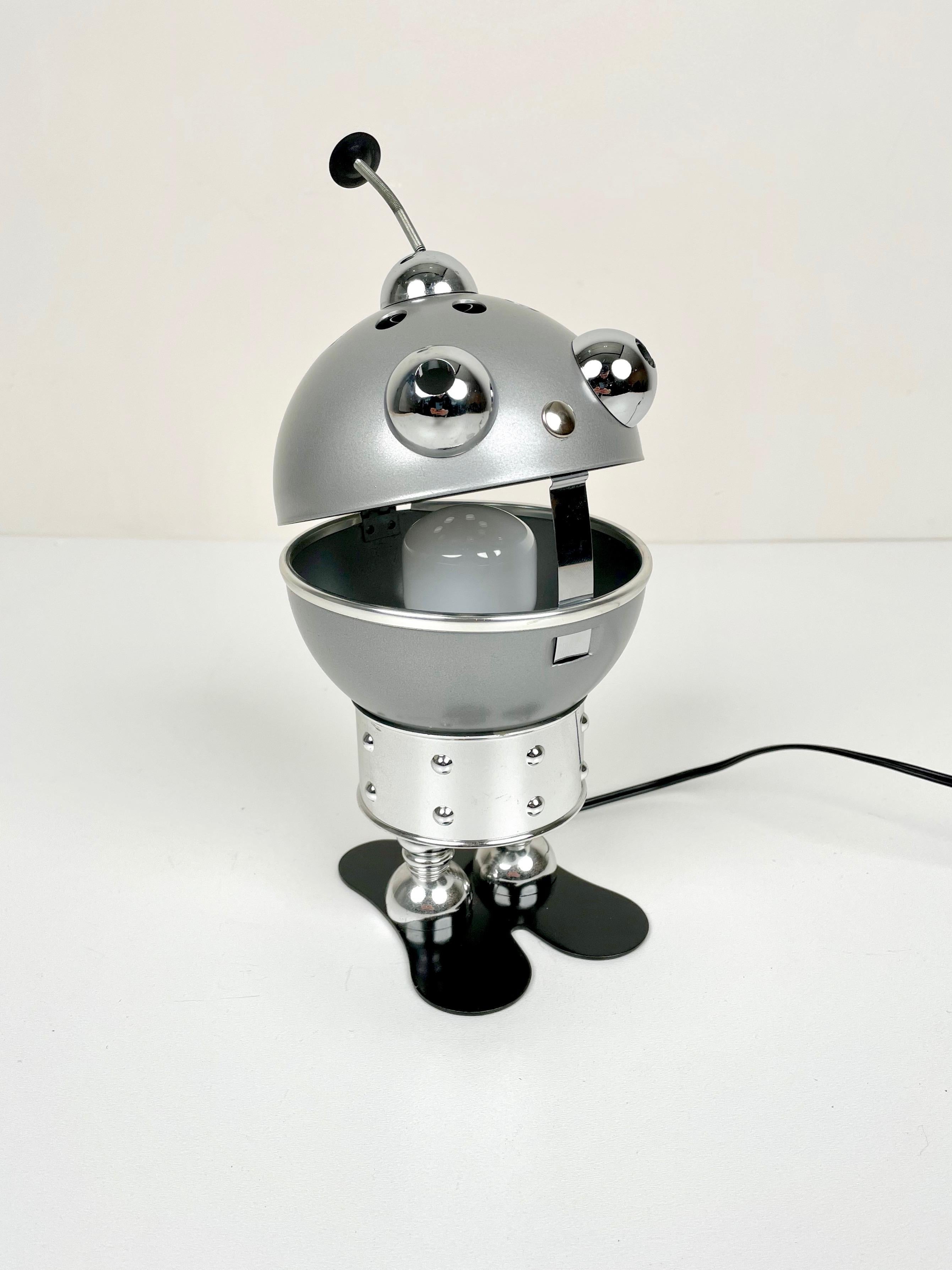 This adorable little robot lamp from the Space Age (1970s) is made of chrome and aluminum. The light comes from its mouth: it makes more or less light depending on the opening of the mouth.