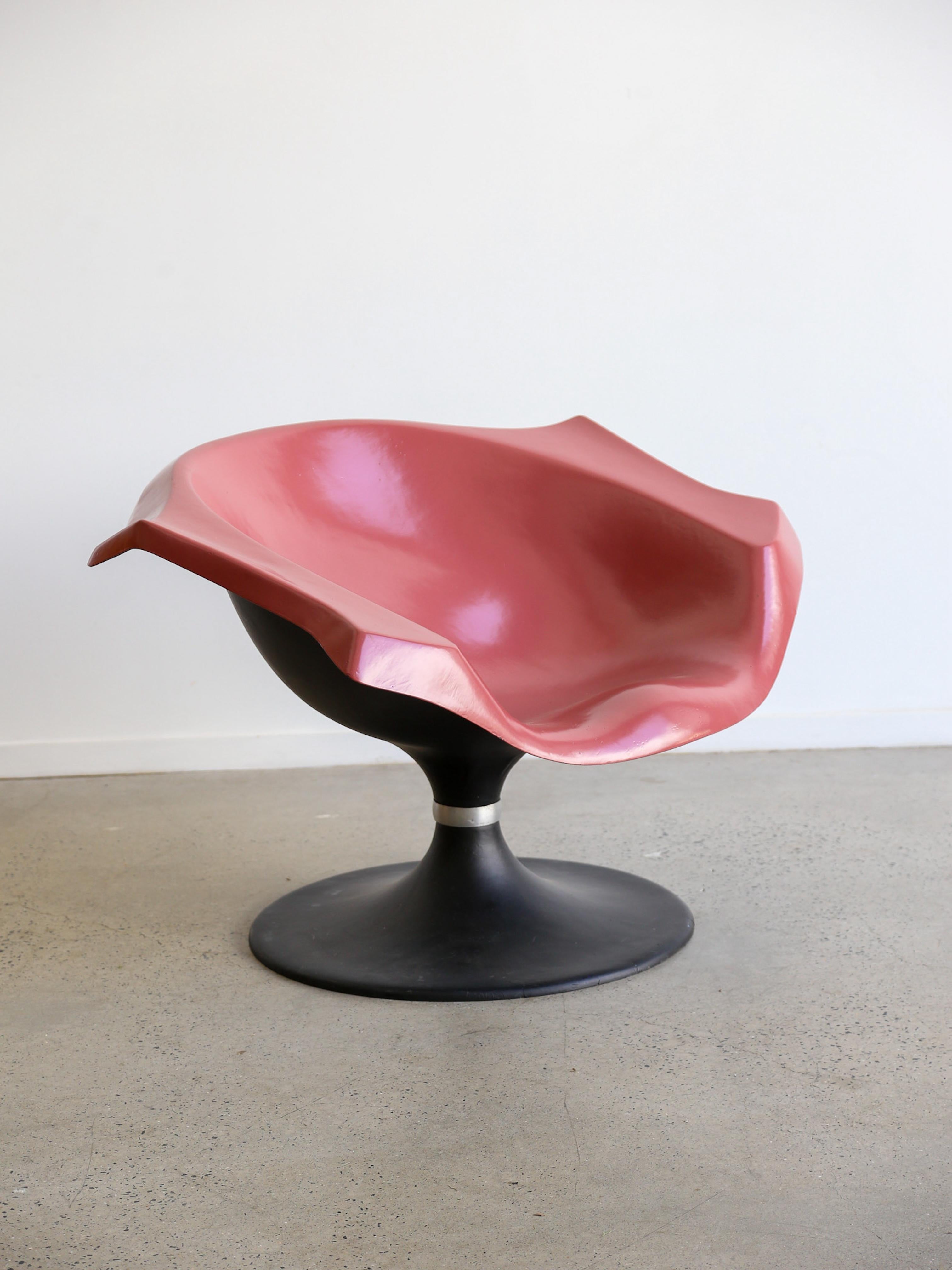 NO AGE, chaise sculpturale au design épuré et futuriste. La chaise présente une assise rose brillante et audacieuse avec une forme unique et incurvée ressemblant à une fleur abstraite ou à un coquillage. La base est noire, robuste et arrondie,
