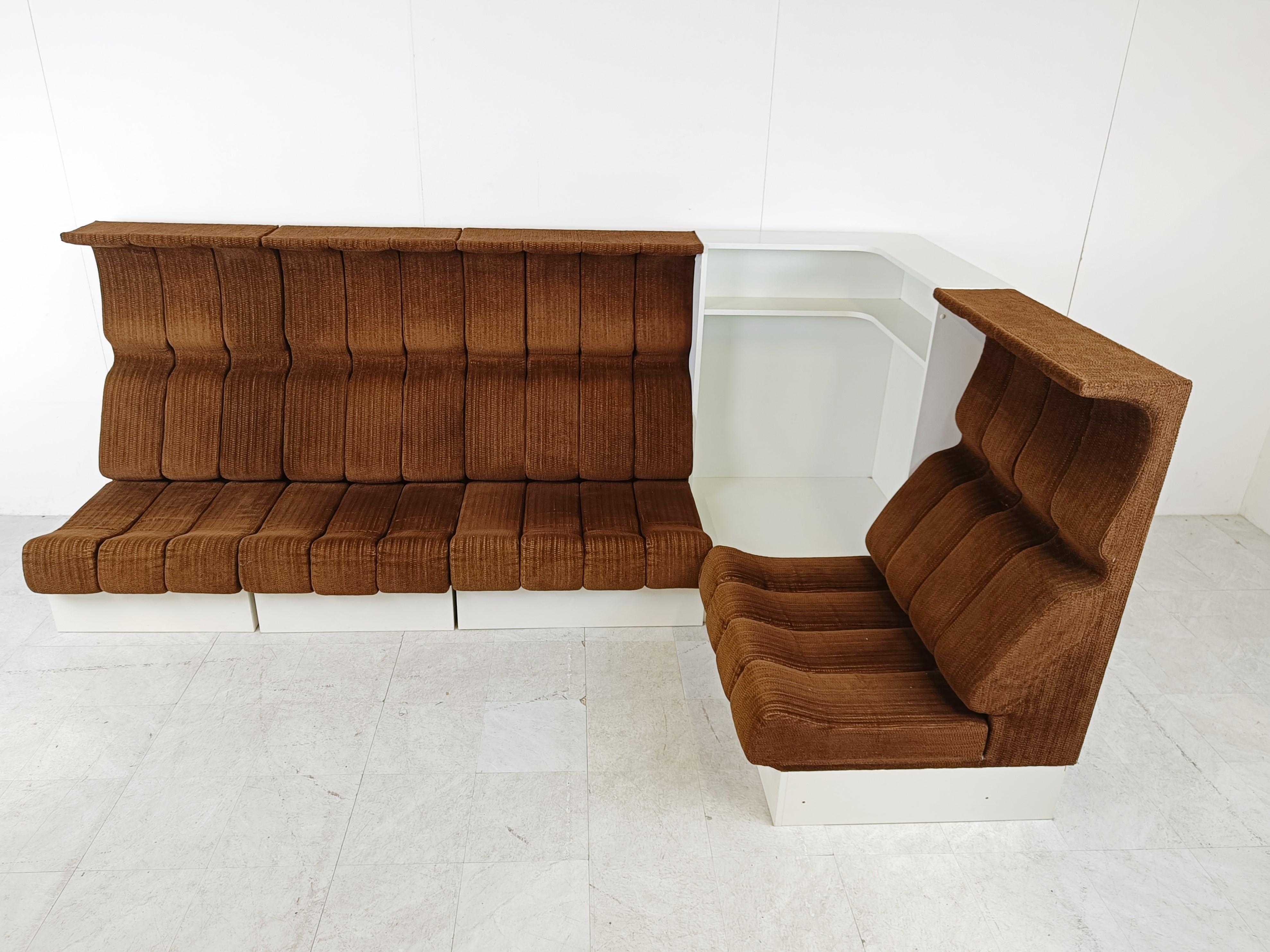 Ensemble de canapés ultra rare d'Interlübke avec des sièges en tissu marron et des bases en bois blanc.

L'ensemble est complété par une pièce d'angle en bois qui sert d'espace de rangement.

Le design du dossier haut est très unique.

Les canapés