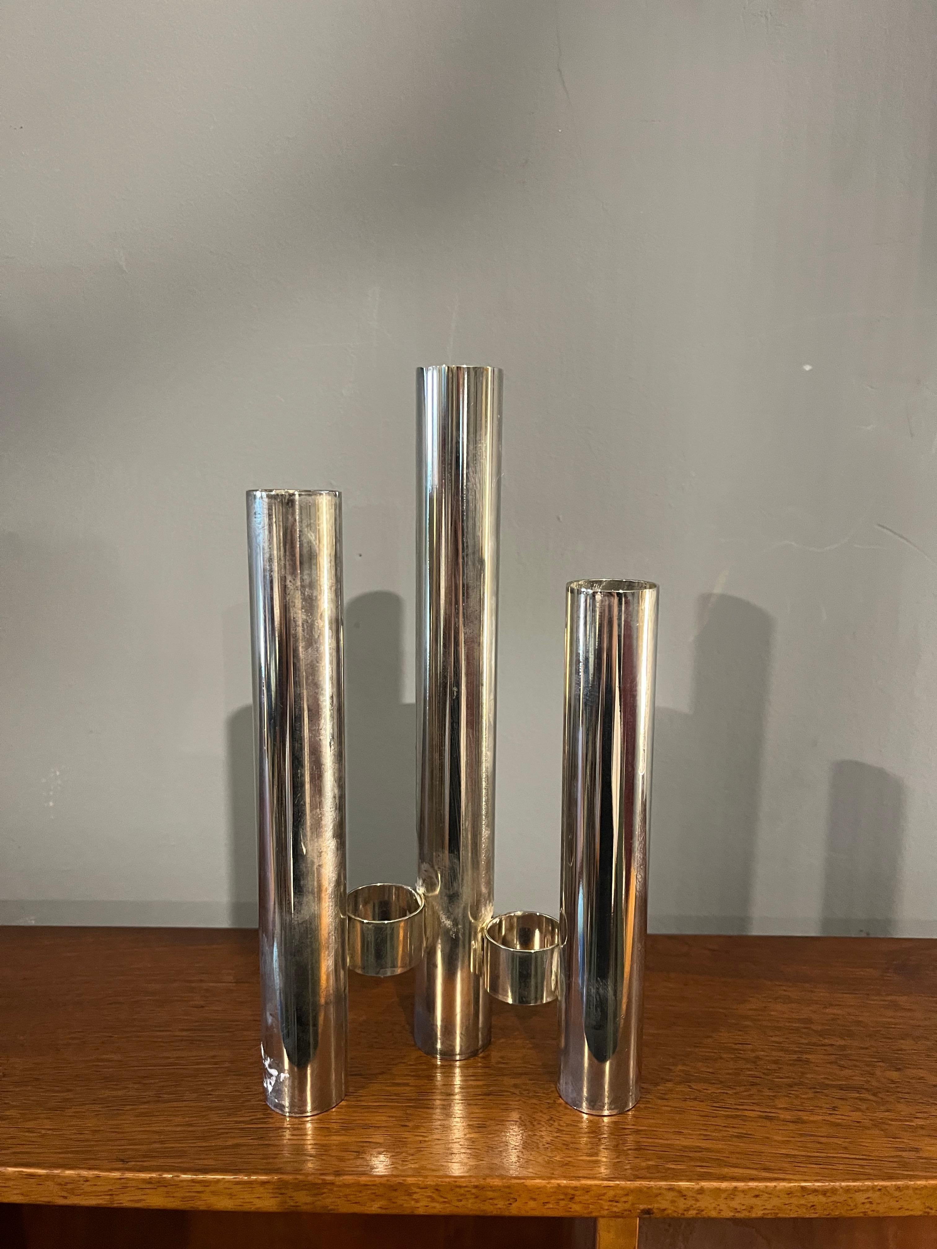 I am selling an elegant vintage candlestick in chromed metal with a modern and minimalist design, probably dating back to the 70s or 80s. The structure is composed of three cylinders of different heights, connected to the base by a geometric system