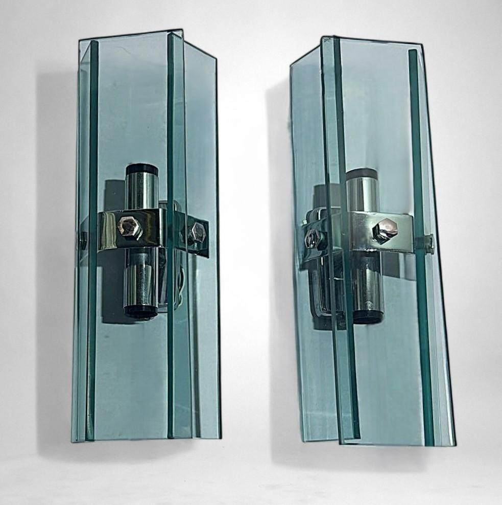Elegantes und geradliniges Paar italienischer Wandleuchter im Vintage-Stil. Jedes Stück besteht aus einem massiven, verchromten Metallrahmen, der drei fein geformte, rechteckige Scheiben aus gehärtetem Glas trägt: eine überlappt die beiden anderen,