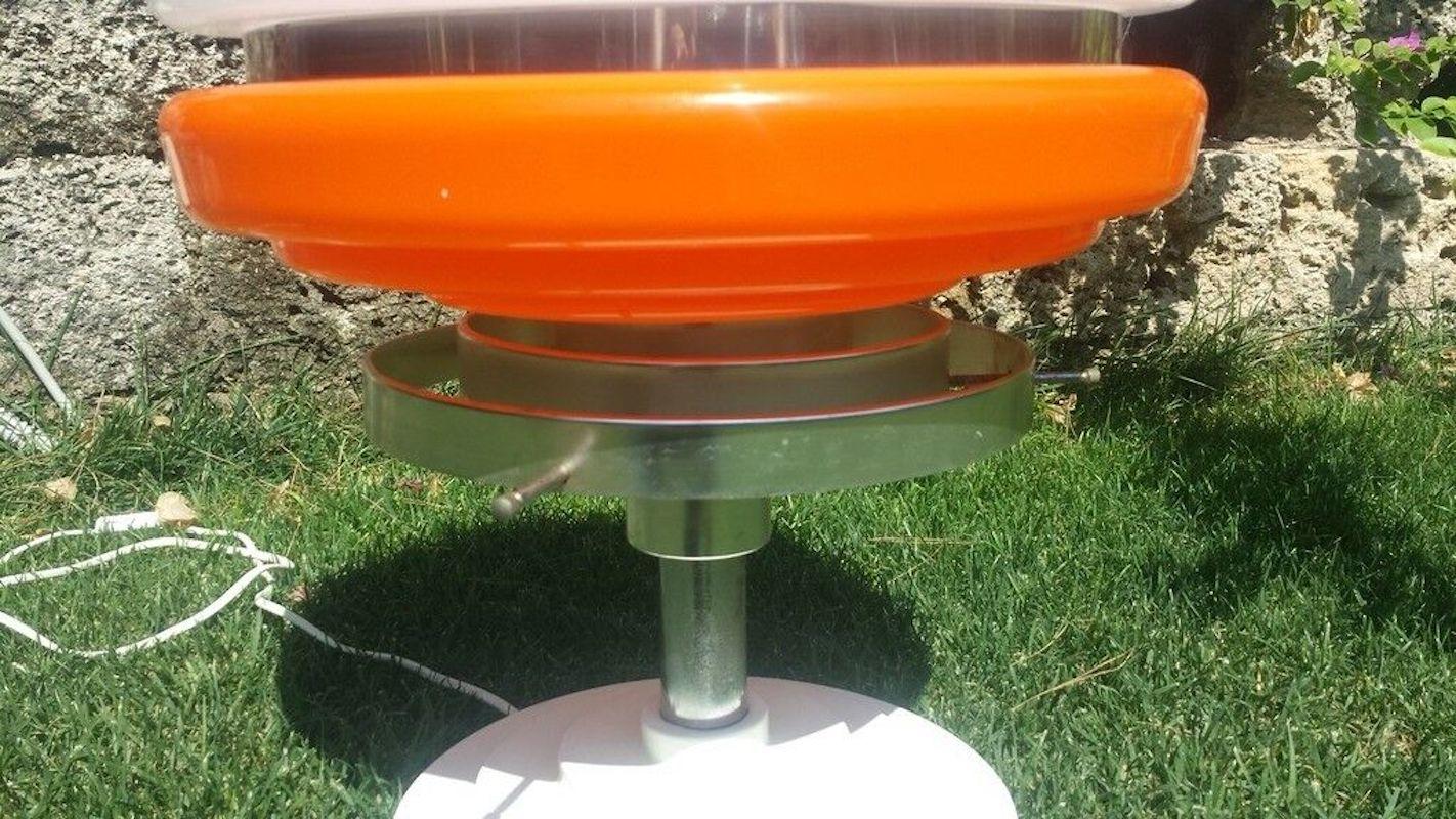This is a wonderful and very rare original table lamp from the 70s, in full space age with an aluminum base and white and orange plexiglass diffuser, the typical colors of the renovation, a large stepped flying saucer with an aggressive and