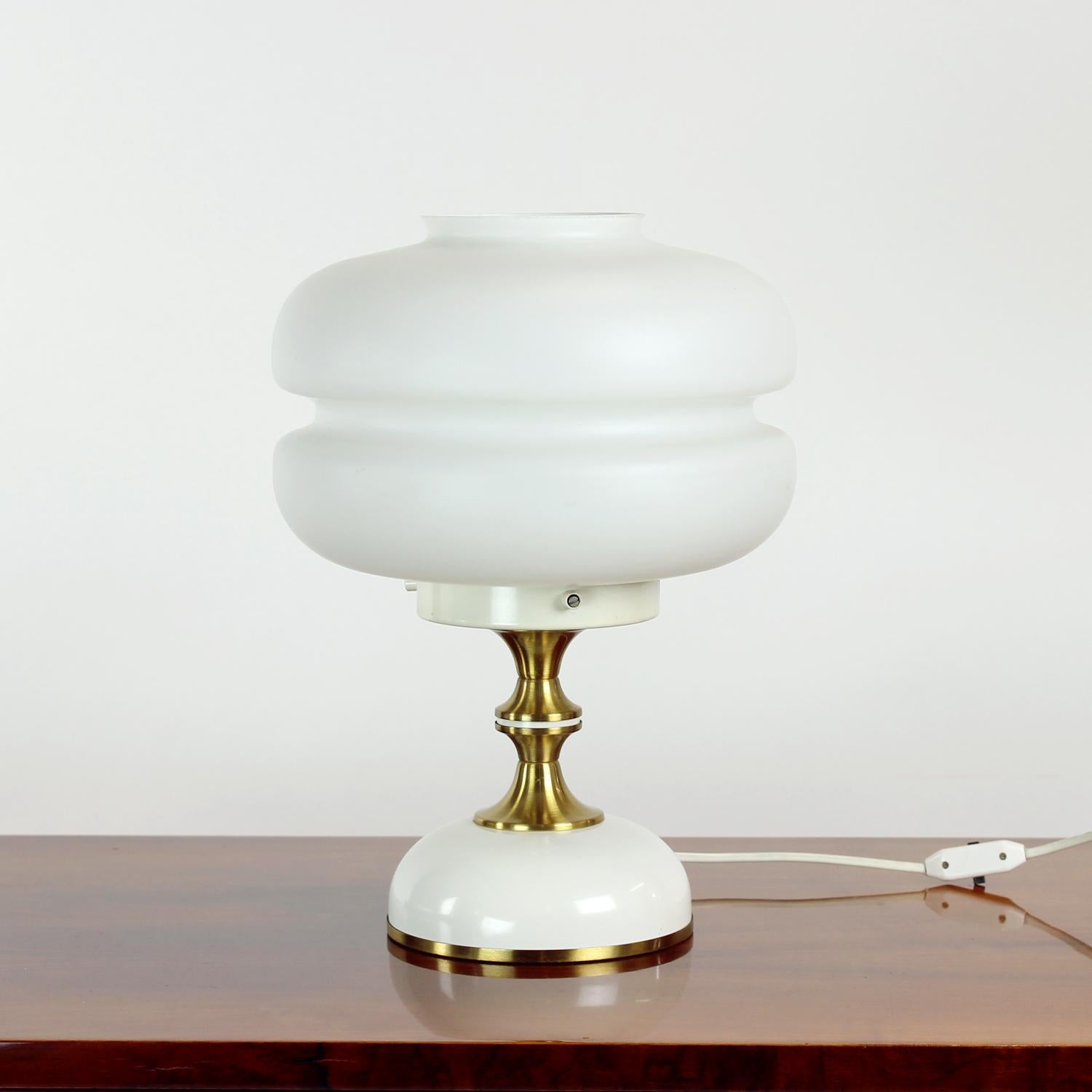 Beautiful vintage table lamp produced by Napako in 1970s. The original label still attached. The lamp is created in the influence of the Space age period of the Czech design. The lamp has a cream-white metal base with brass details. The shield is in