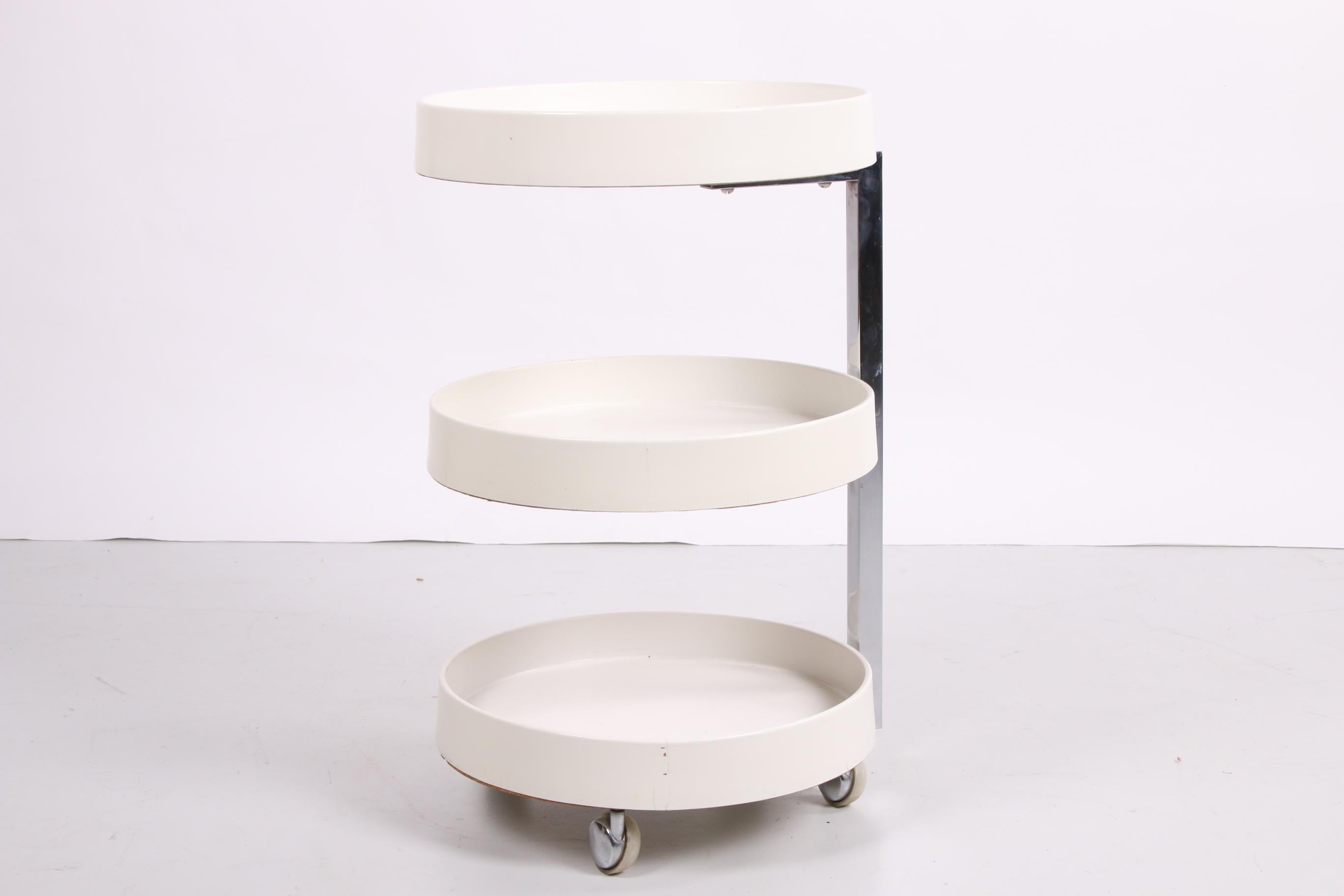 This is a white trolley from the Space Age time. The nice design also makes it good to use as a side table.

Made of white plastic. The trolley has a beautiful appearance due to the combination of the white color with the chrome of the original