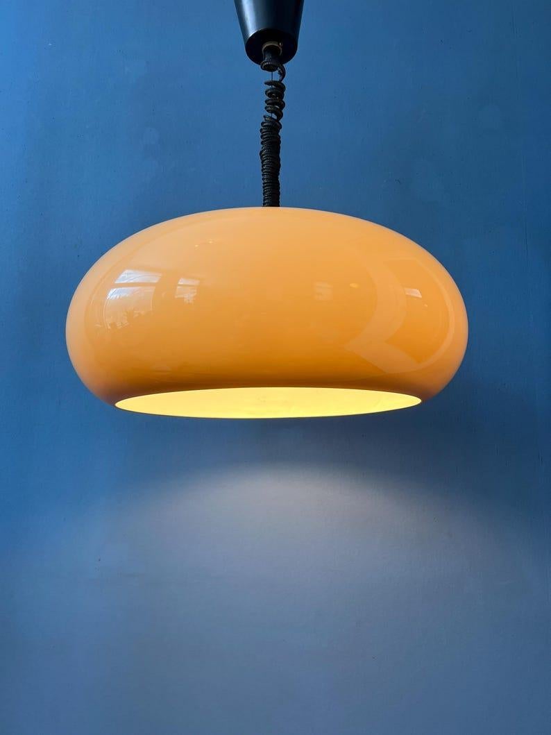 Lampada a sospensione dell'era spaziale in vetro acrilico a forma di UFO in colore beige caffè. Il paralume in plexiglass produce una luce calda. L'altezza della lampada può essere facilmente regolata grazie al meccanismo di sospensione. La lampada
