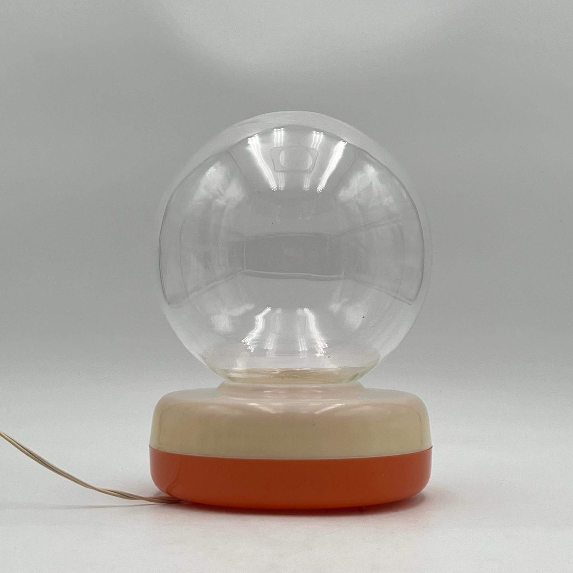 Distinctive and very rare lamp with a beige / orange plastic base holder topped by a big clear glass bowl.

The base made of translucent plastic contains a soft E14 bulb for ambient lighting. The glass globe is equipped with a plastic support that